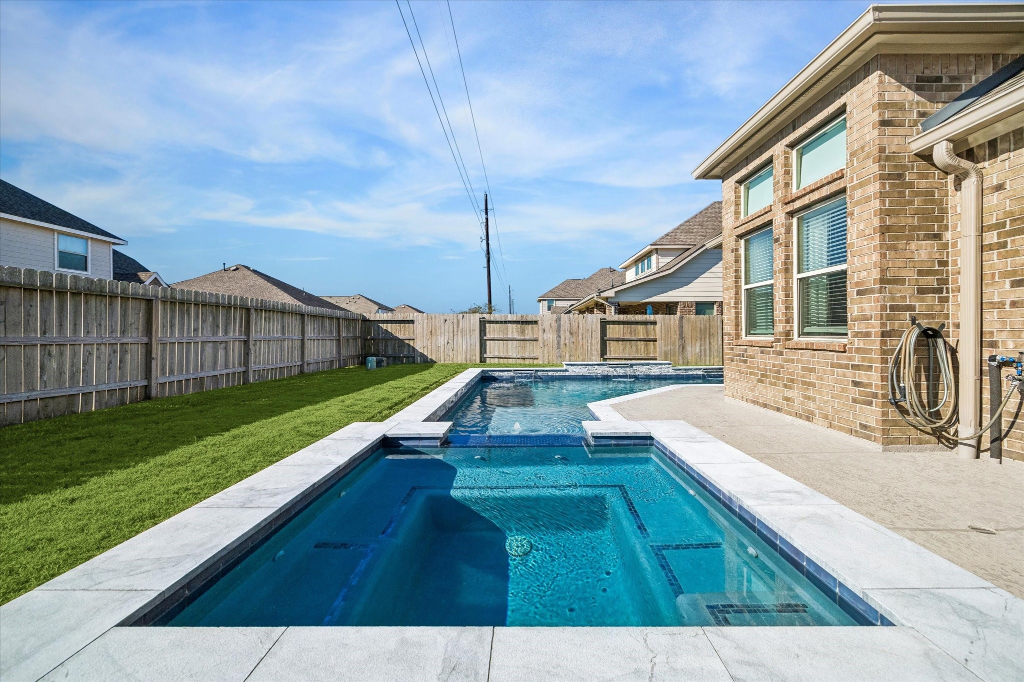 Stacked-stone accents and sheer-descent water features bring a custom touch to the pool, while the nearby covered patio and open lawn complete this inviting outdoor setting.
