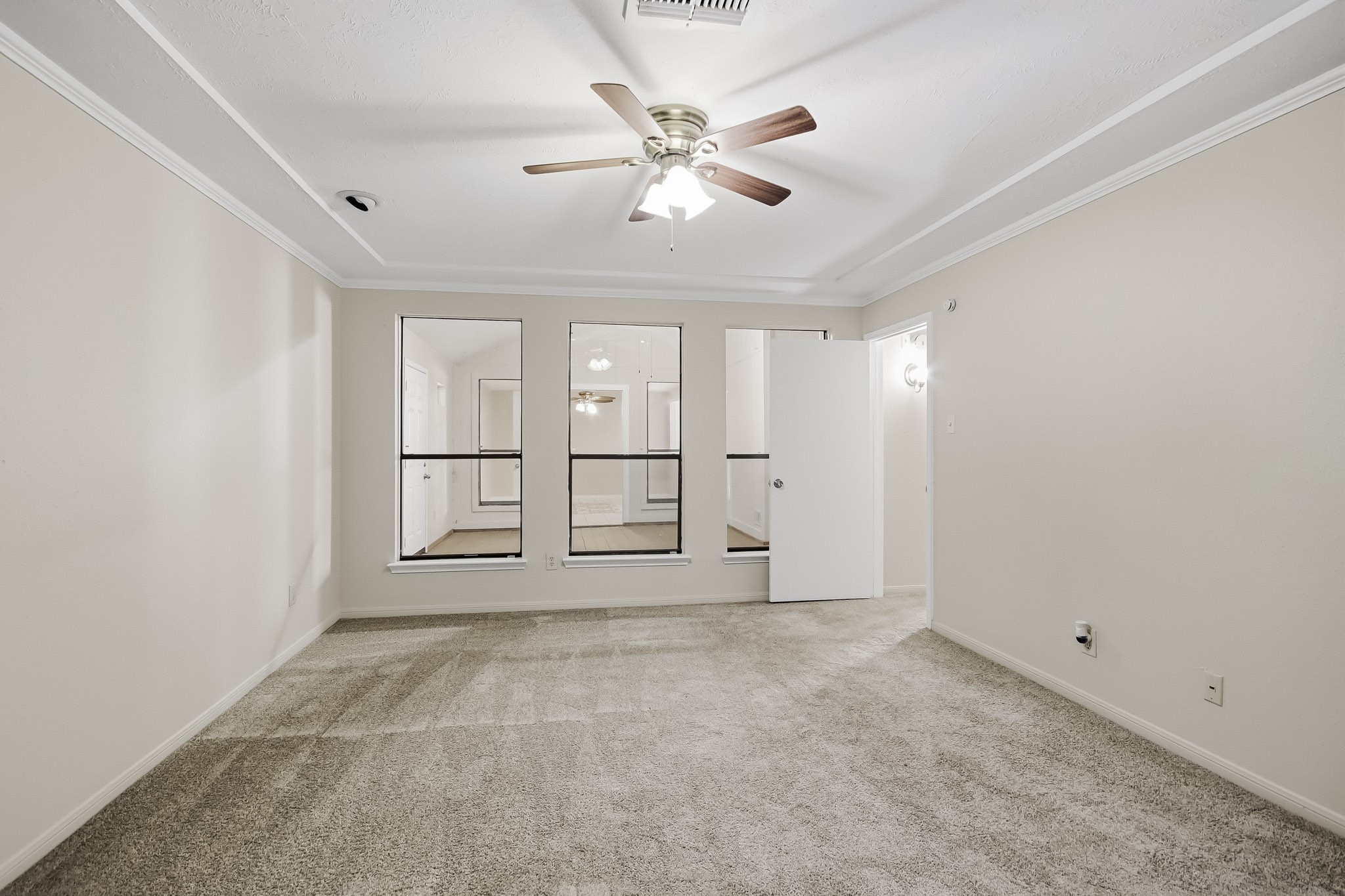Another view of the spacious primary bedroom, featuring a tray ceiling, access to ensuite bathroom, and a view of the adjoining flex space.