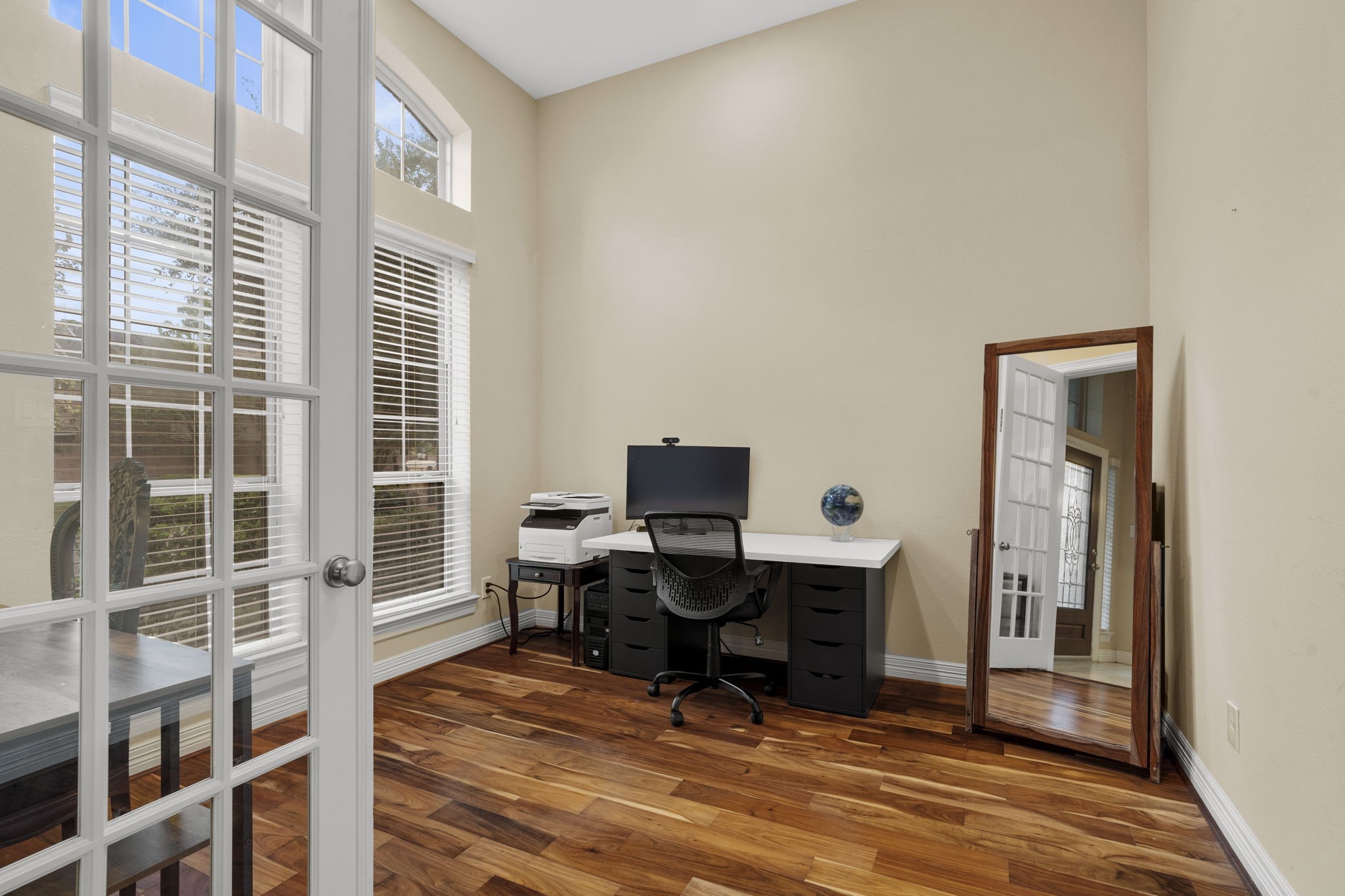 French doors open to a private home office at the front of the home, featuring high ceilings and a wall of windows.