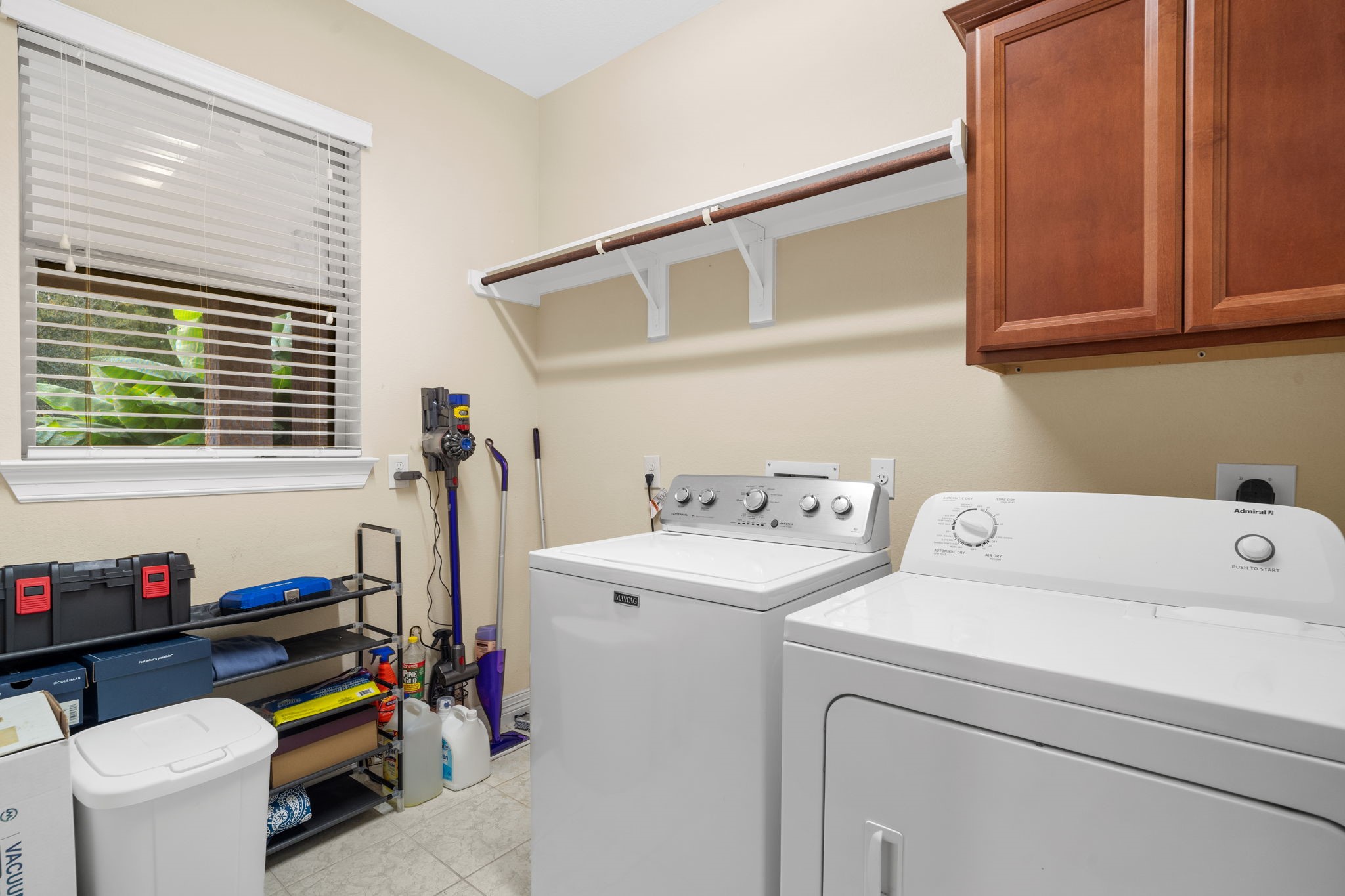 Convenient in-home laundry room with a storage cabinet, hanging rack, shelf, and space for a full-sized refrigerator.