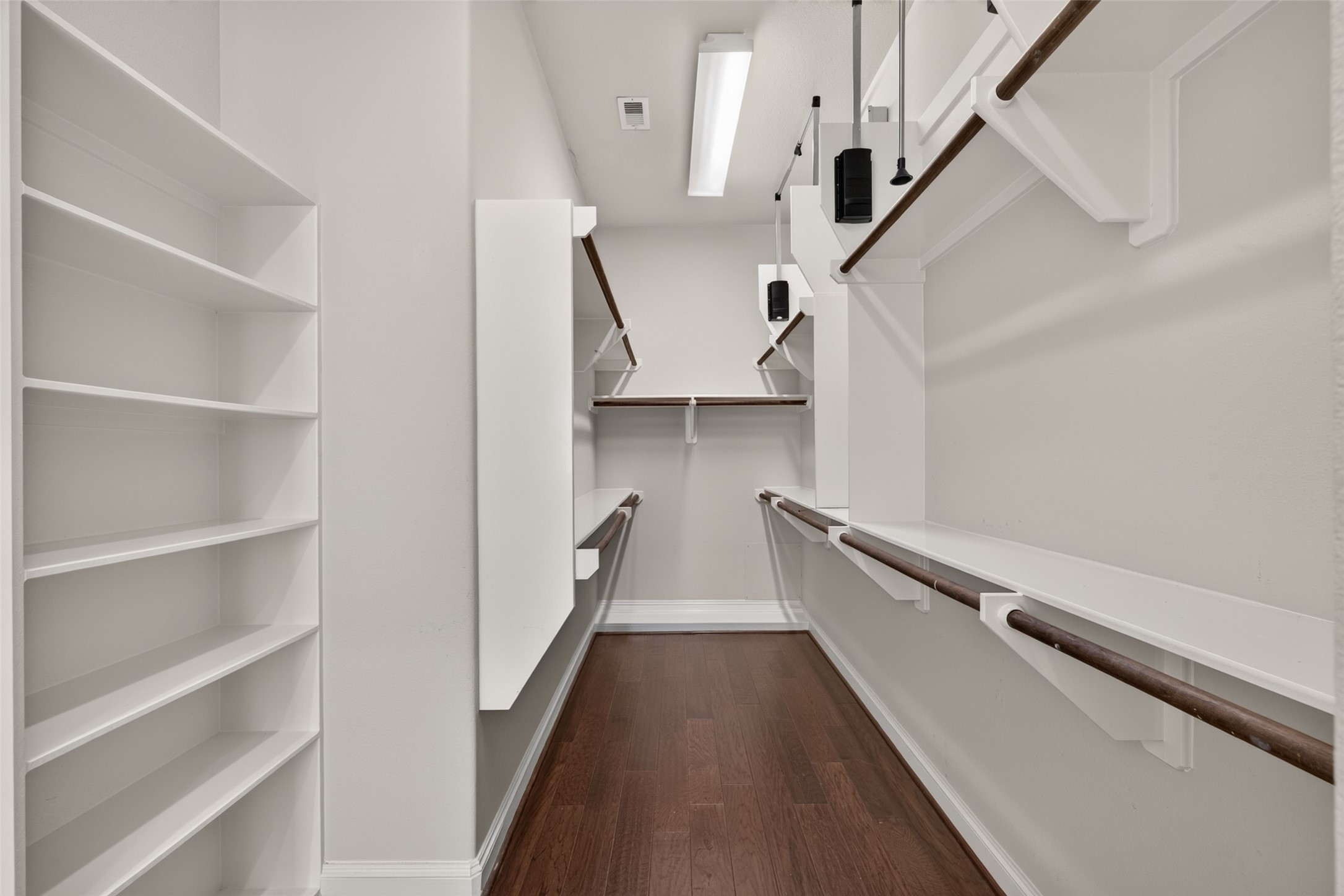 Spacious walk-in closet with ample shelving and hanging space, featuring sleek wooden floors and bright overhead lighting.