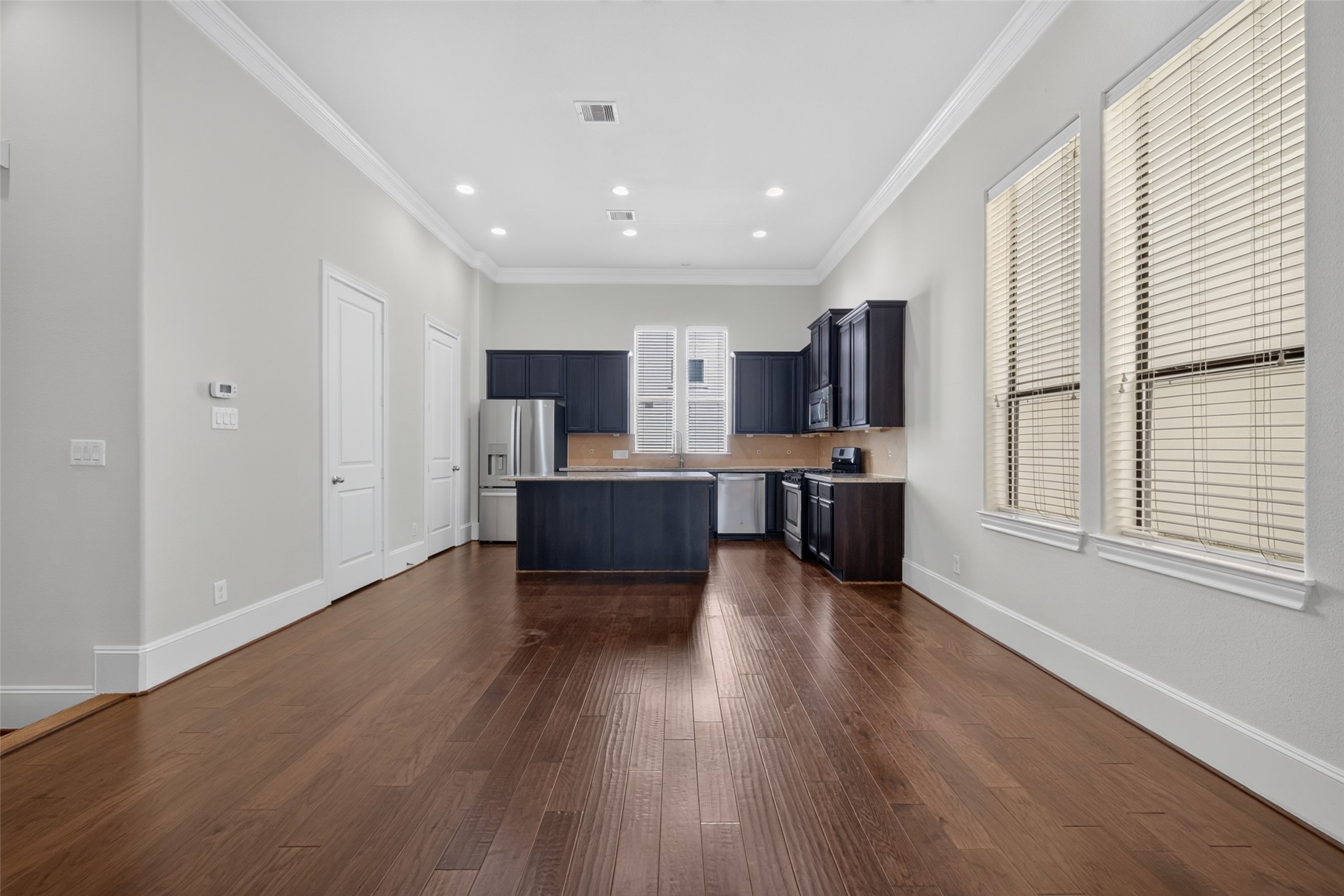 Spacious kitchen with elegant dark cabinetry, stainless steel appliances, and rich hardwood flooring, all bathed in natural light from large windows.