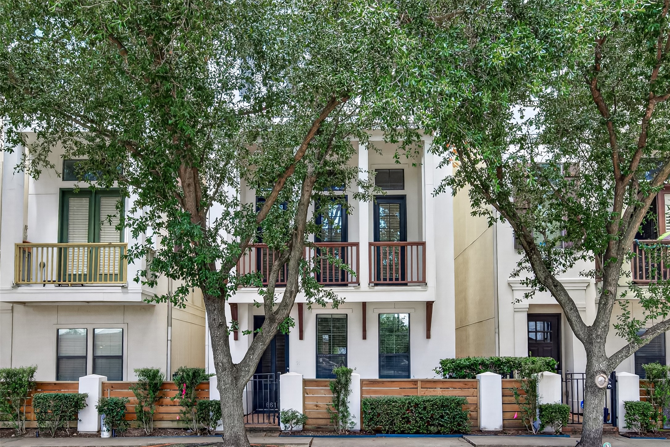 Charming townhouse with a welcoming facade, featuring large windows and a private balcony, nestled among mature trees for added privacy and shade. Charming townhouse with a welcoming facade, featuring large windows and a private balcony, nestled among mature trees for added privacy and shade.