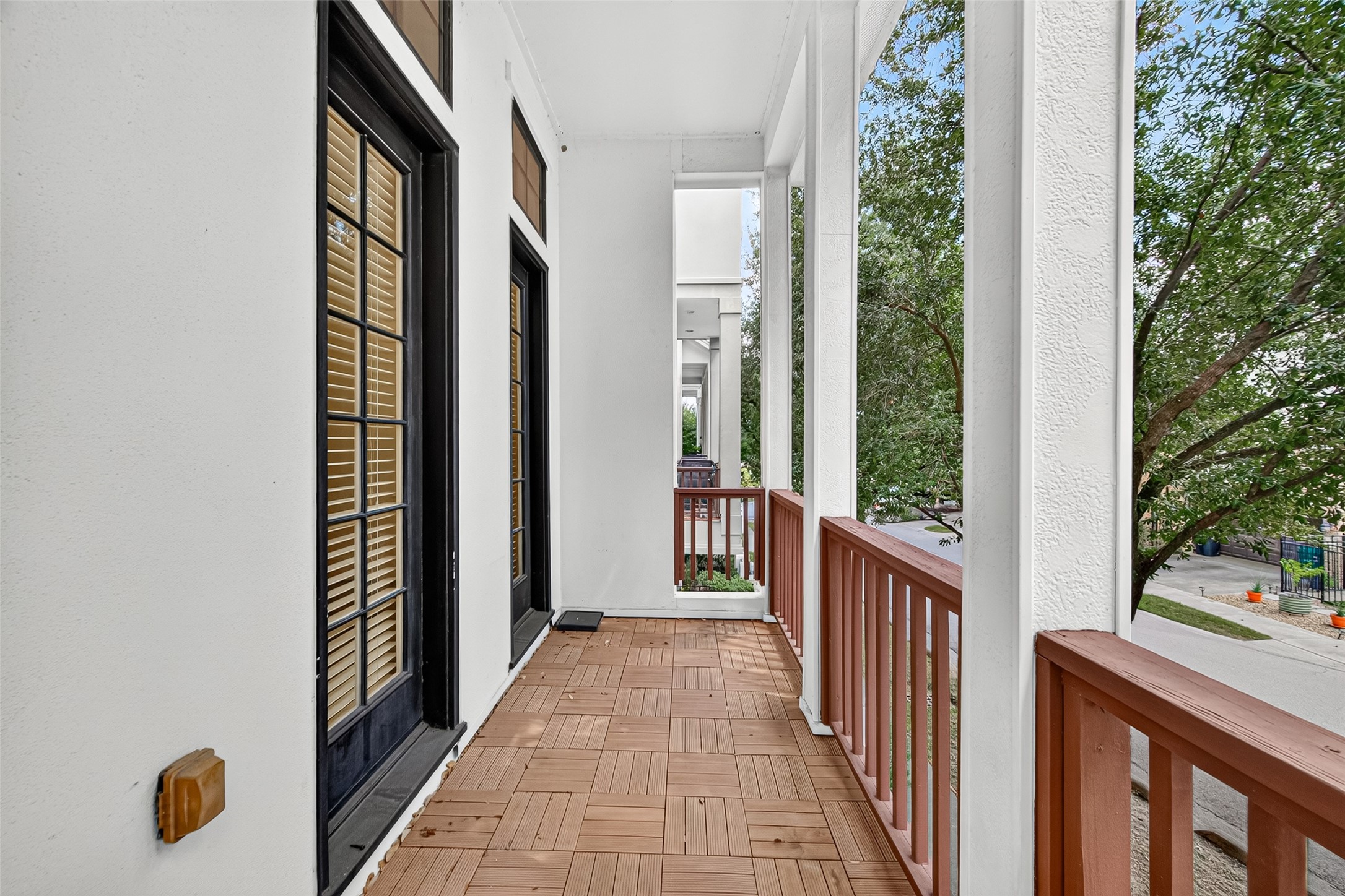 Charming covered balcony with classic French doors, offering a serene outdoor space with lush tree views.