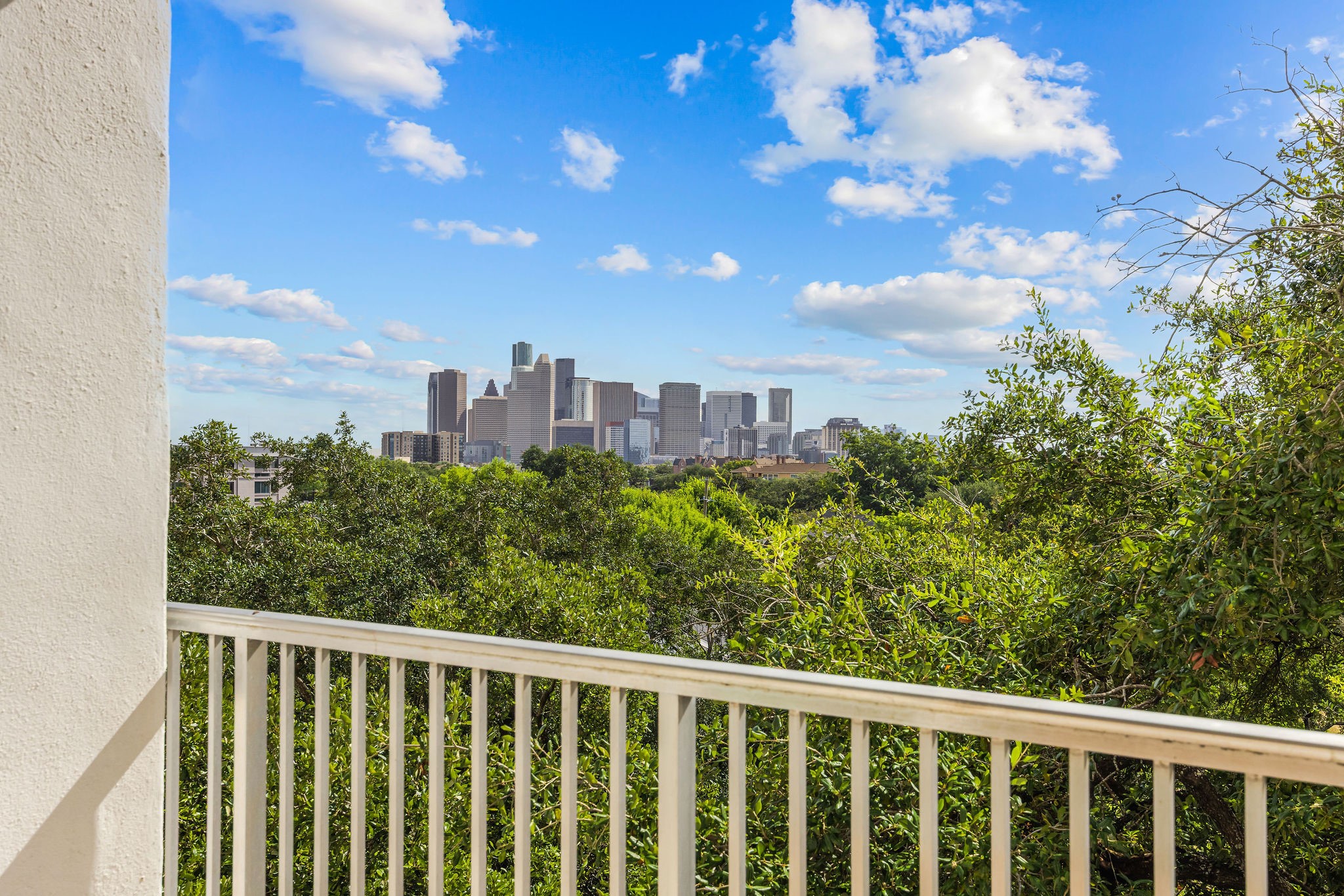 Enjoy stunning city skyline views from this spacious balcony, surrounded by lush greenery for a serene oasis.