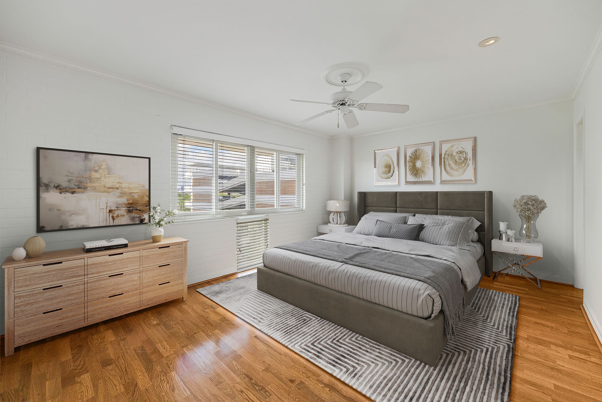 This virtually staged photo shows a spacious and bright bedroom featuring hardwood floors, a stylish bed, and elegant decor, complemented by ample natural light from large windows.