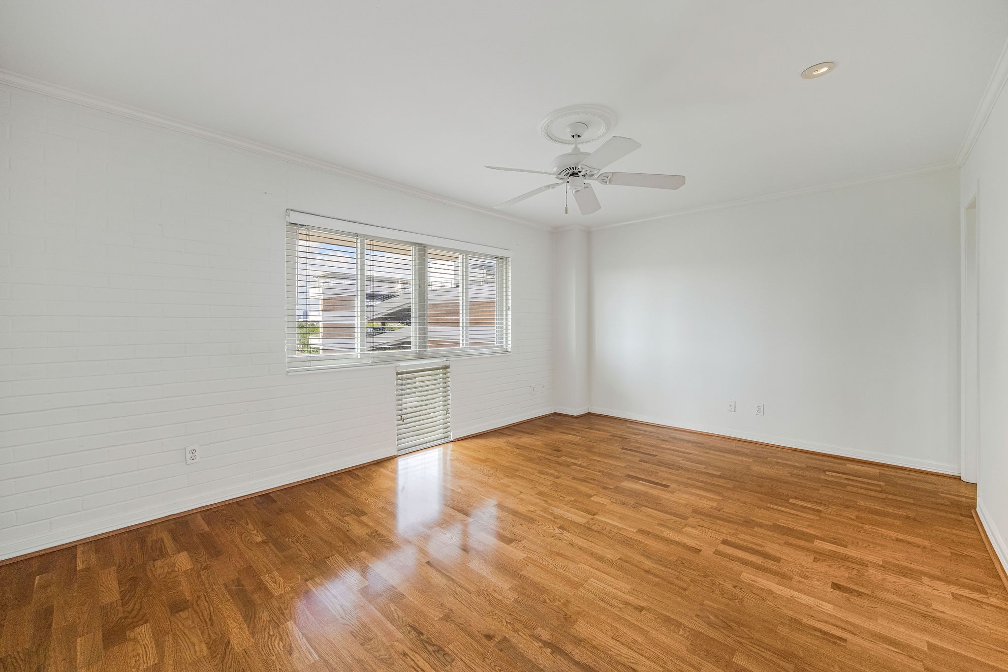 Bright and spacious bedroom with gleaming hardwood floors, large windows for natural light, and a ceiling fan for comfort.