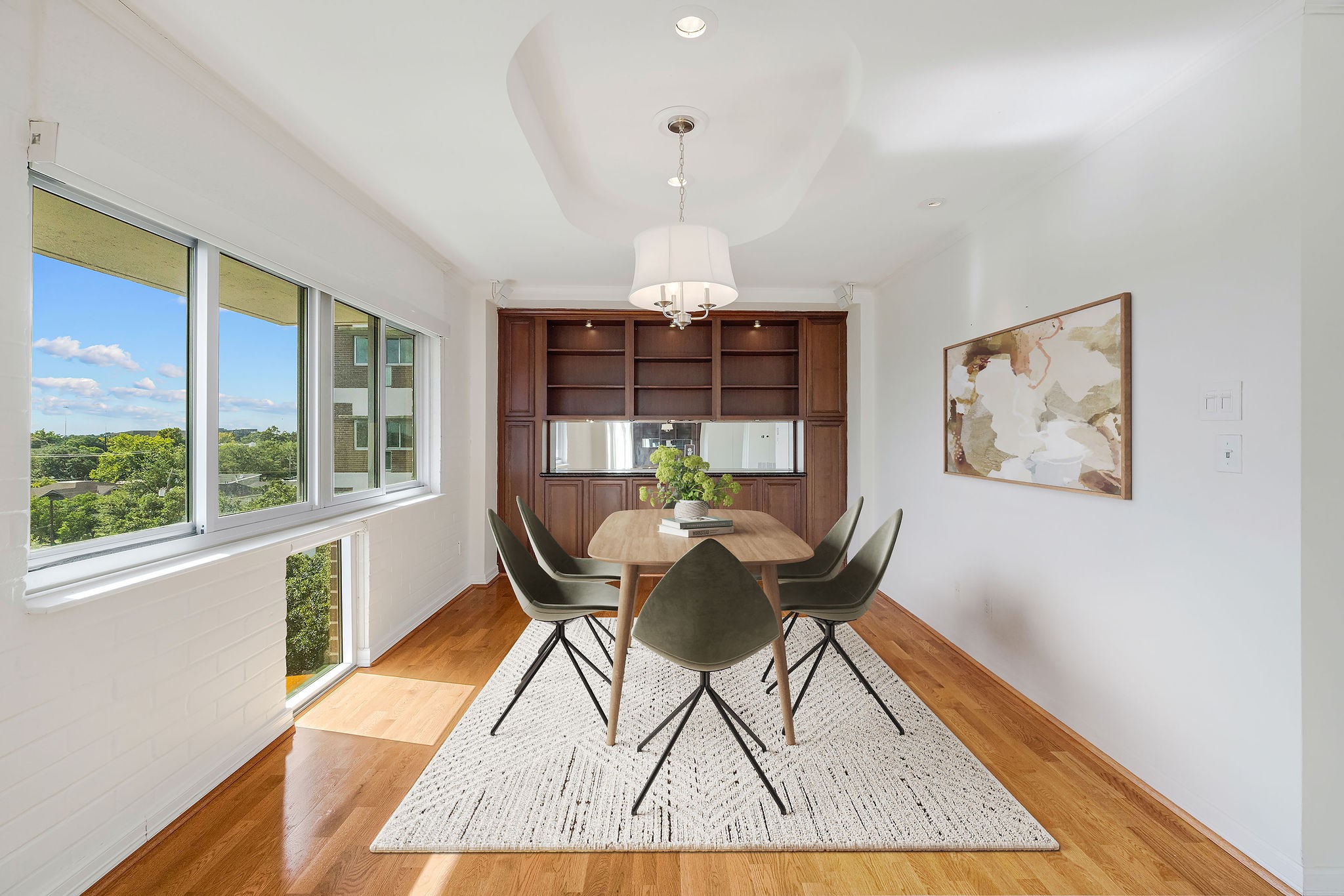 This virtually staged photo shows off a bright dining area with expansive windows, hardwood floors, and modern lighting perfect for entertaining.