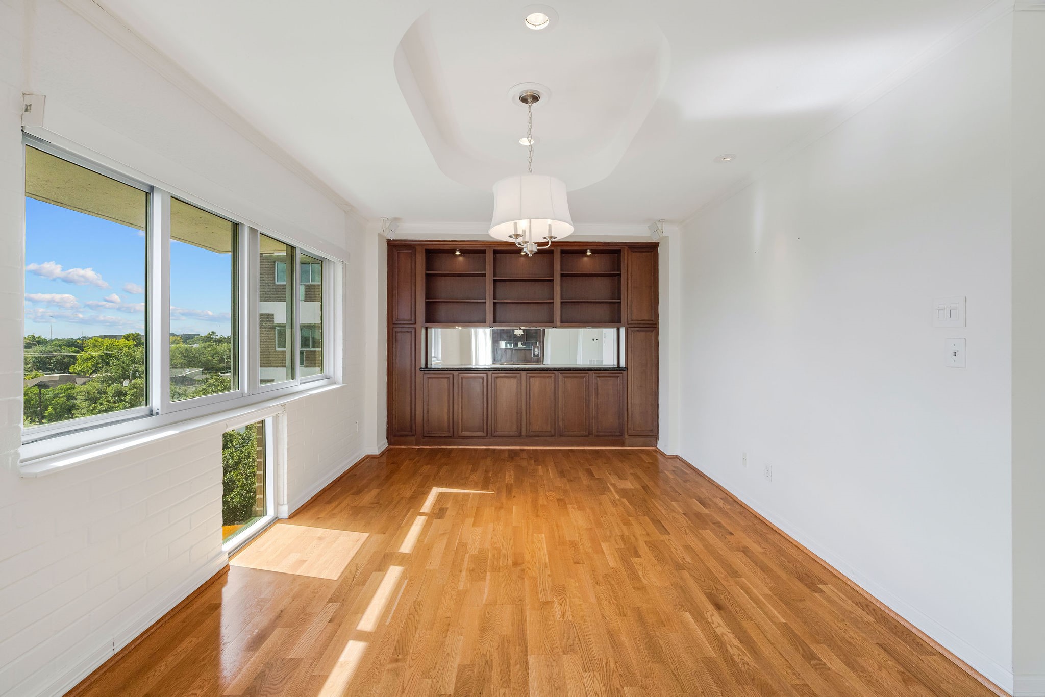 Bright and airy room with large windows offering scenic views, complemented by warm hardwood floors and elegant built-in shelving.