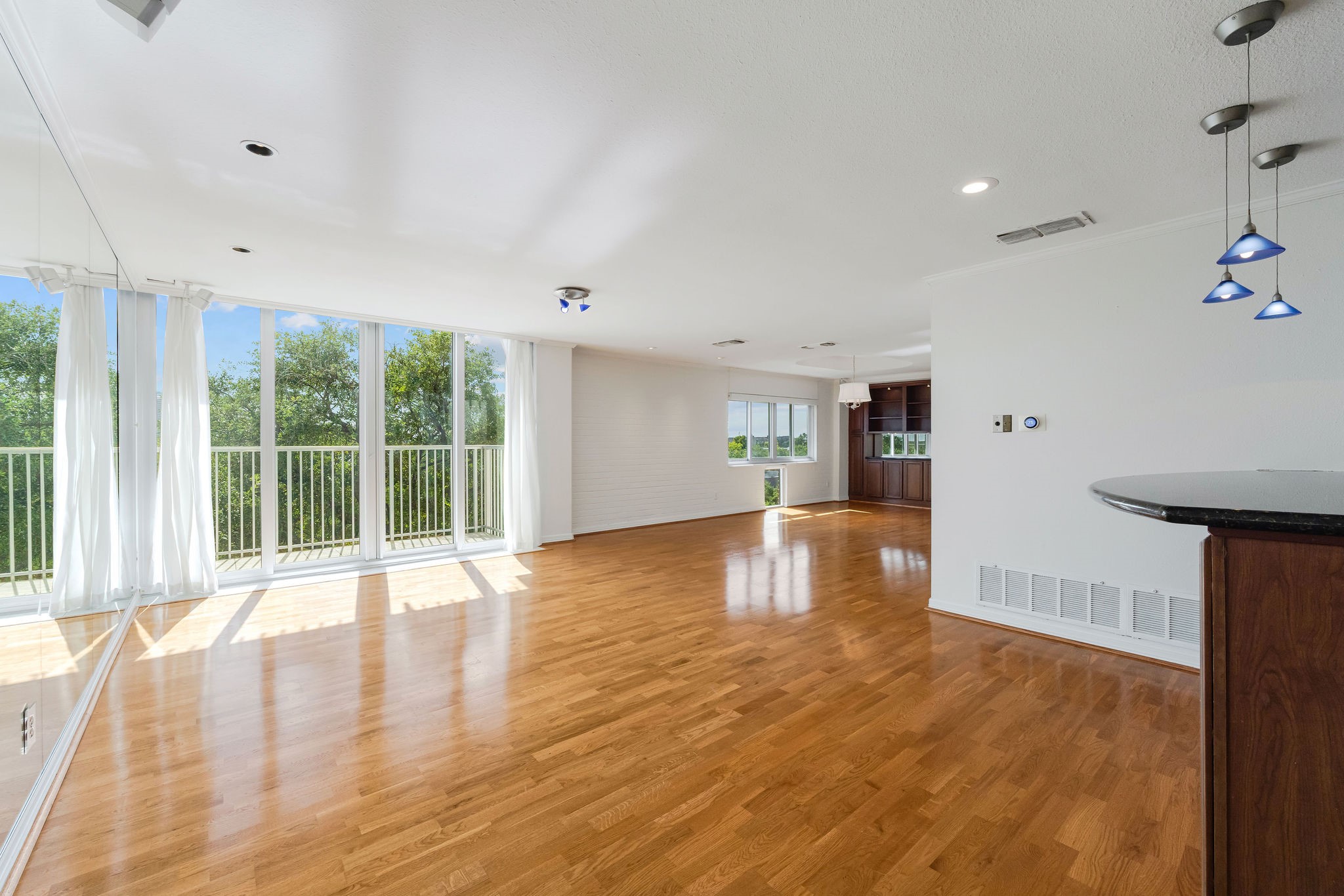 Spacious open-plan living area with hardwood floors, abundant natural light from large windows, and modern pendant lighting.
