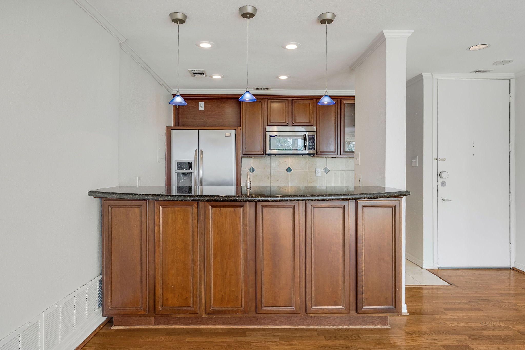 Charming kitchen with rich wooden cabinetry, sleek granite countertops, and modern stainless steel appliances, highlighted by elegant pendant lighting.