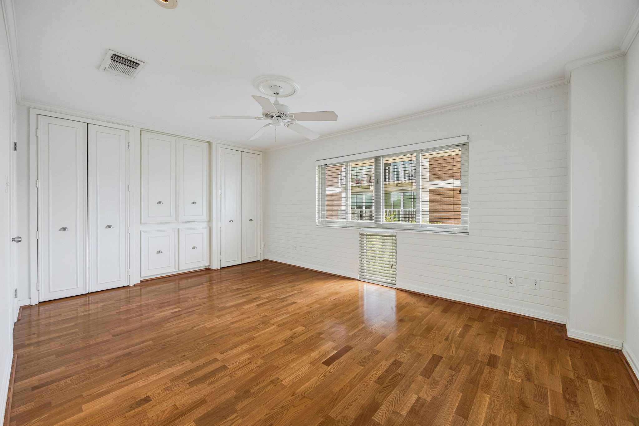Spacious bedroom with gleaming hardwood floors, abundant natural light from wide windows, and ample storage with built-in cabinetry.
