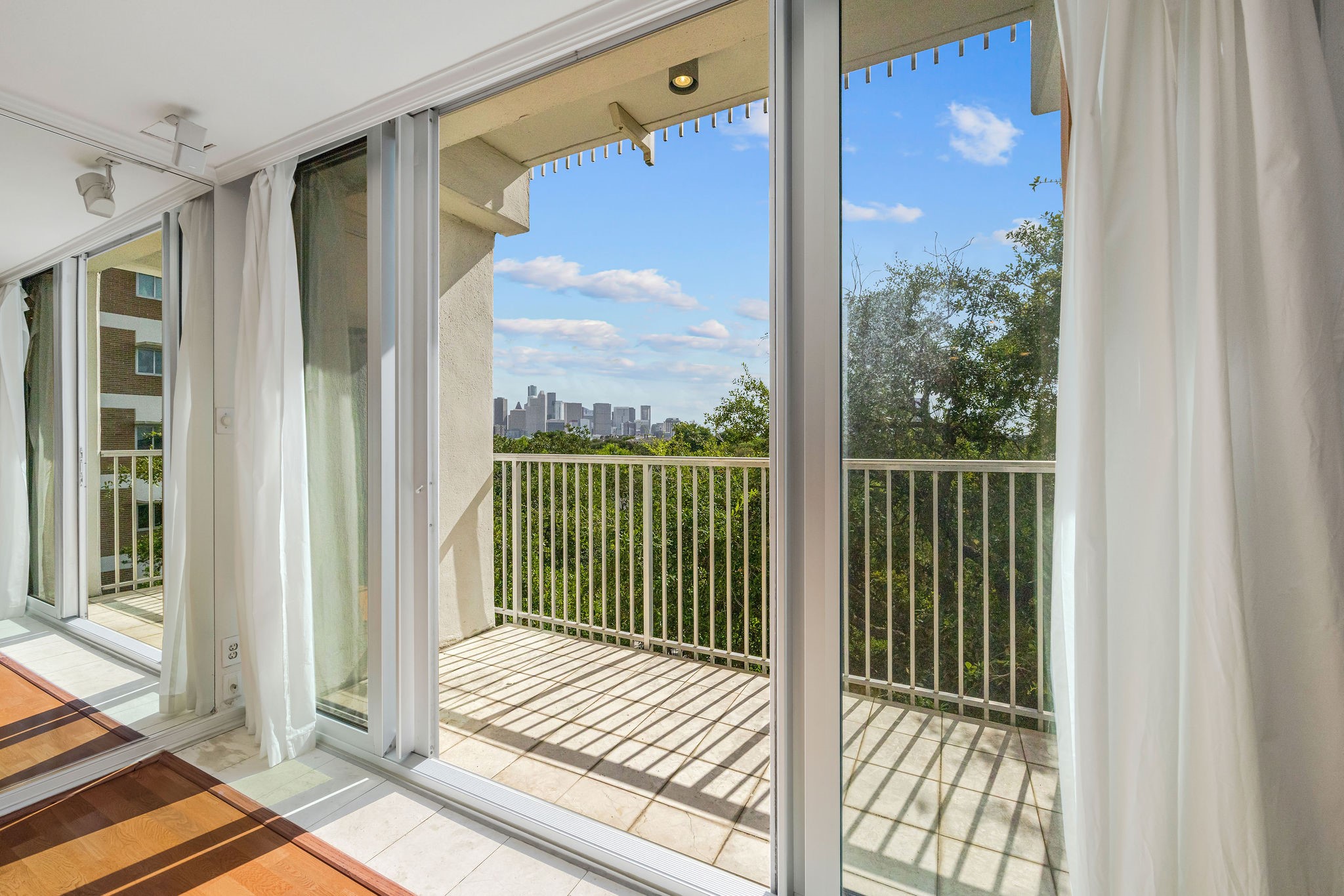 Expansive floor-to-ceiling windows open to a private balcony with stunning city skyline views, offering an abundance of natural light.