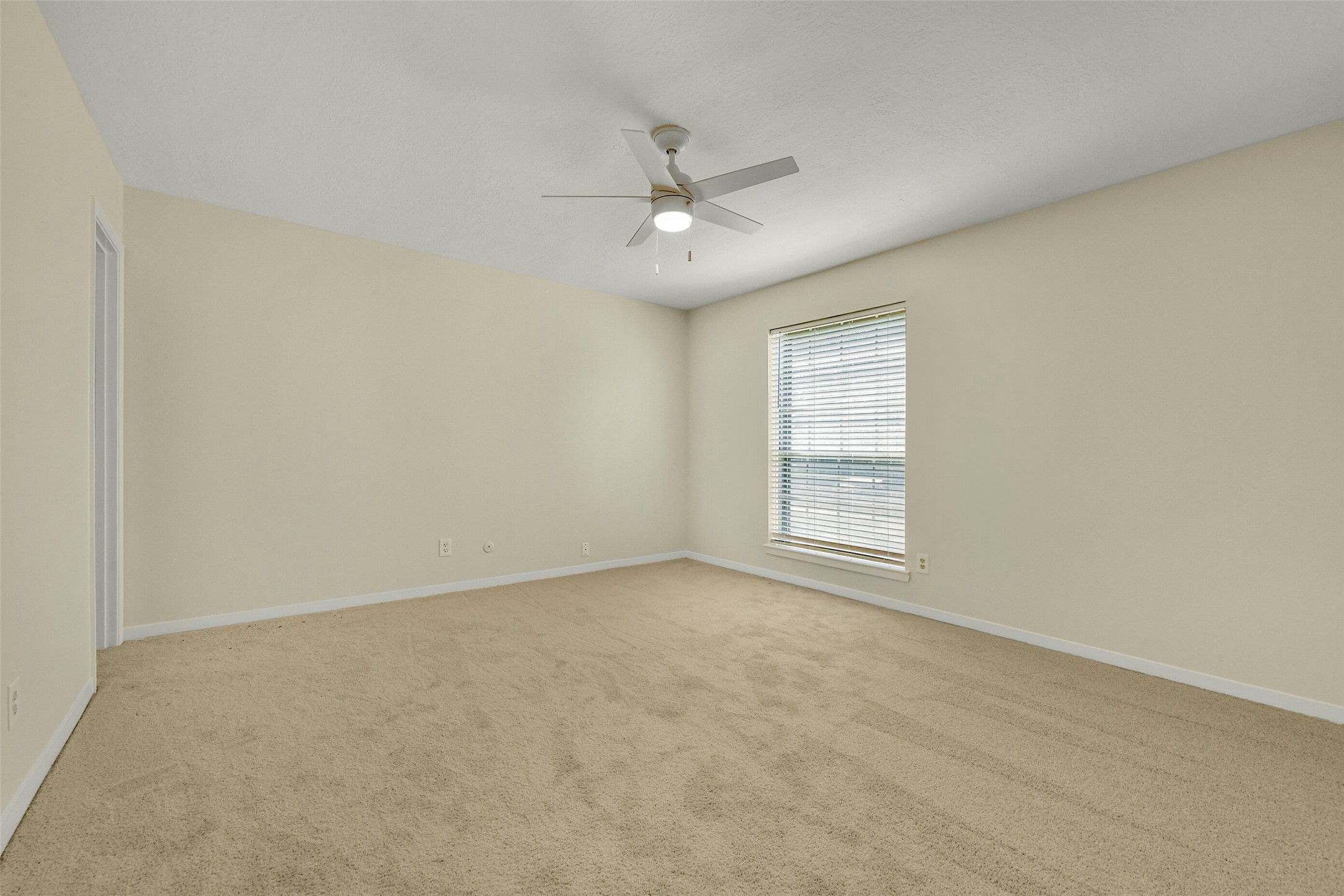 Bedroom with soft carpet flooring, neutral walls, and a large window allowing ample natural light, complemented by a modern ceiling fan for comfort.