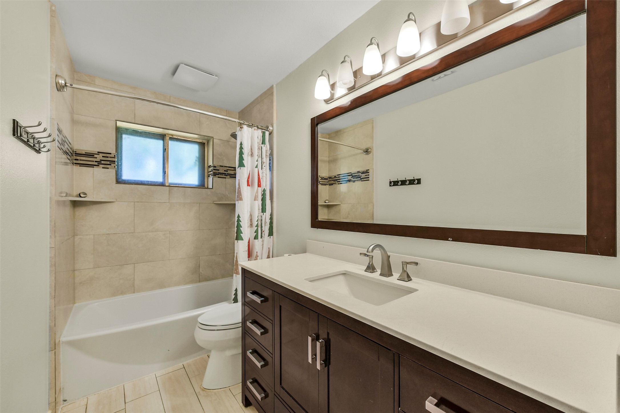 Modern bathroom featuring a sleek vanity with ample storage, elegant lighting, and a tiled shower-tub combo with a decorative backsplash.