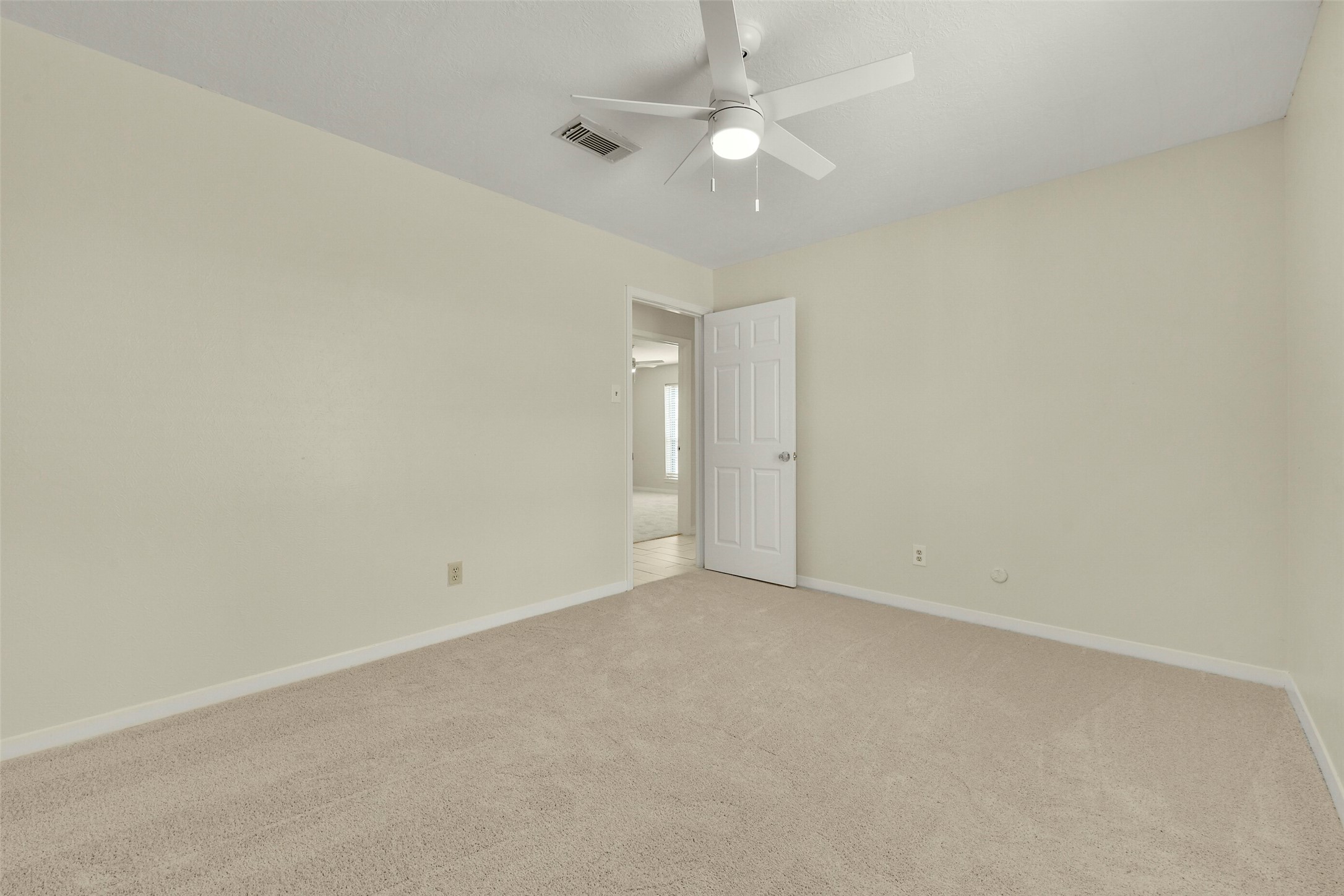 Bright and airy bedroom featuring soft carpeting, neutral walls, and a ceiling fan, providing a comfortable and inviting atmosphere.