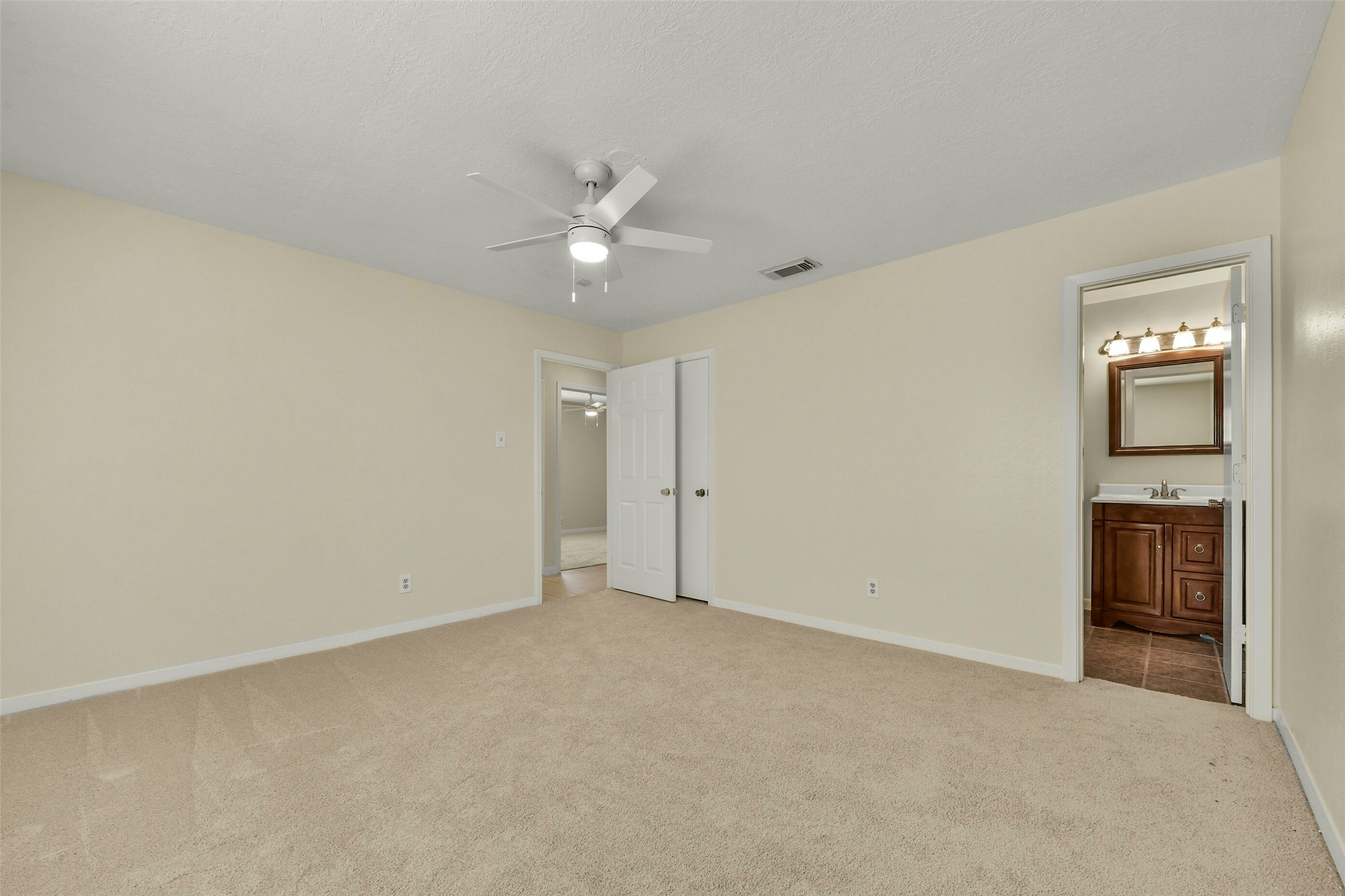 Soft carpet, neutral walls, and a ceiling fan, featuring an ensuite bathroom for added convenience.
