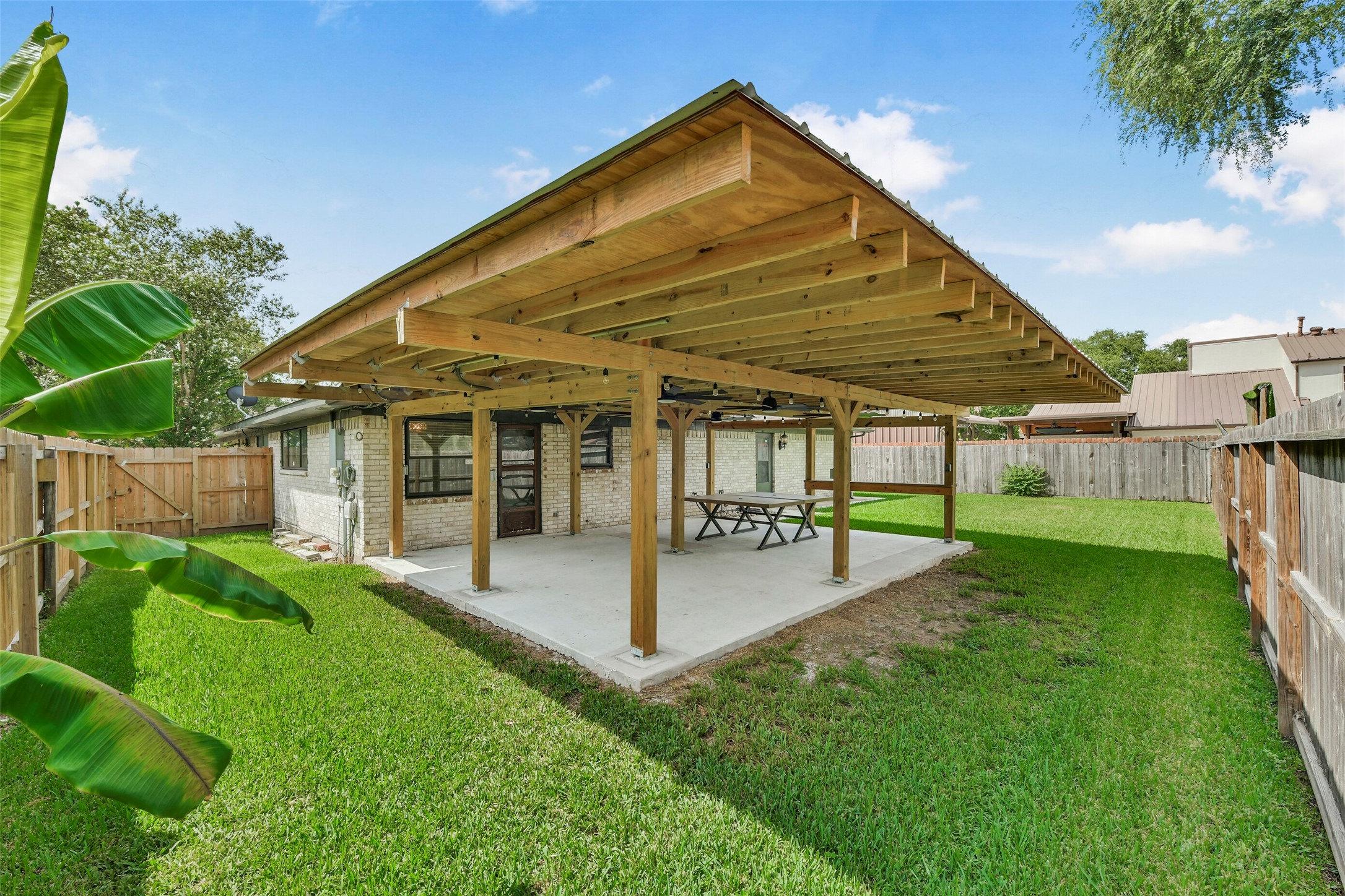 Backyard featuring a large wooden pergola, perfect for outdoor gatherings and relaxation, surrounded by a lush green lawn and privacy fencing.