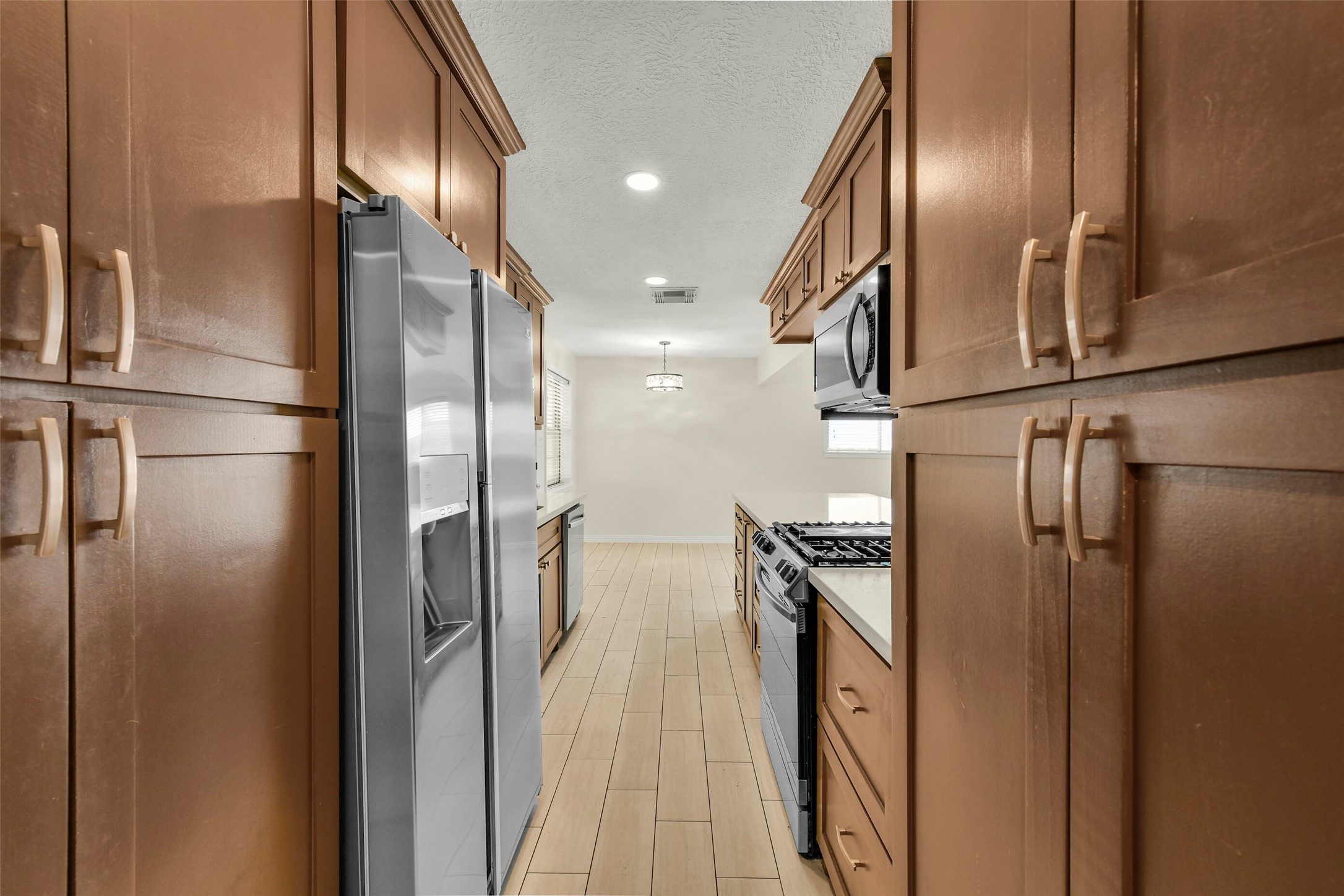 Galley kitchen featuring rich wood cabinetry, modern stainless steel appliances, and sleek tile flooring, offering a perfect blend of functionality and elegance.