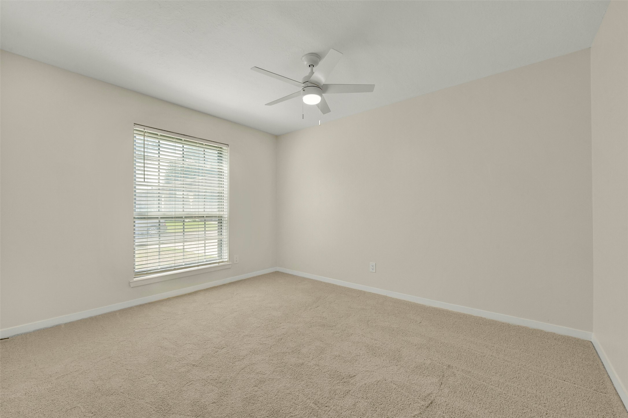 Bedroom featuring neutral walls, plush carpeting, and a ceiling fan, complemented by a large window that allows natural light to pour in.