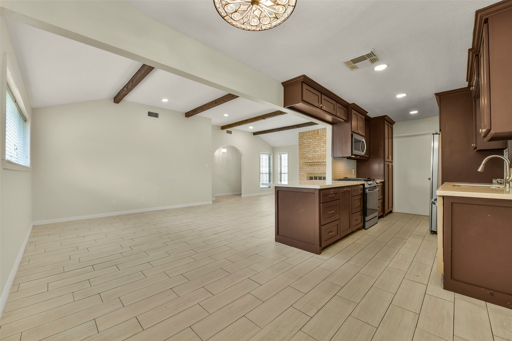 Bright, open-concept living space featuring a modern kitchen with rich cabinetry, stainless steel appliances, and elegant wood-beam accents, perfect for entertaining.