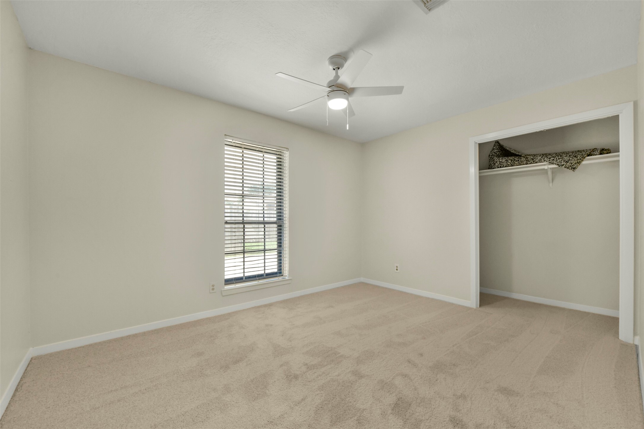 Bedroom featuring soft carpet, a ceiling fan, and a large window for natural light, alongside a convenient open closet.
