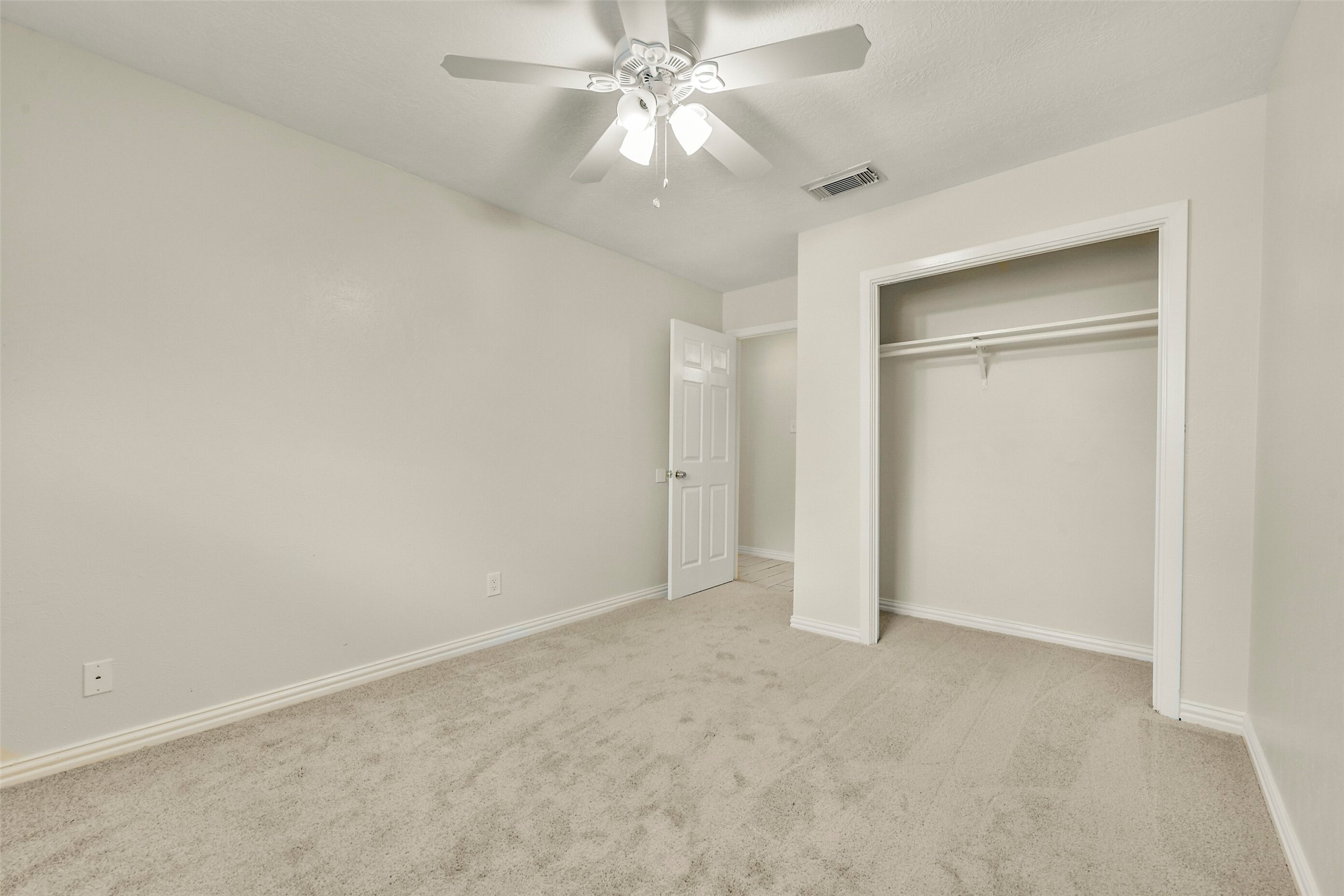 Cozy bedroom with plush carpeting, a ceiling fan, and a spacious closet, offering a comfortable and inviting atmosphere.