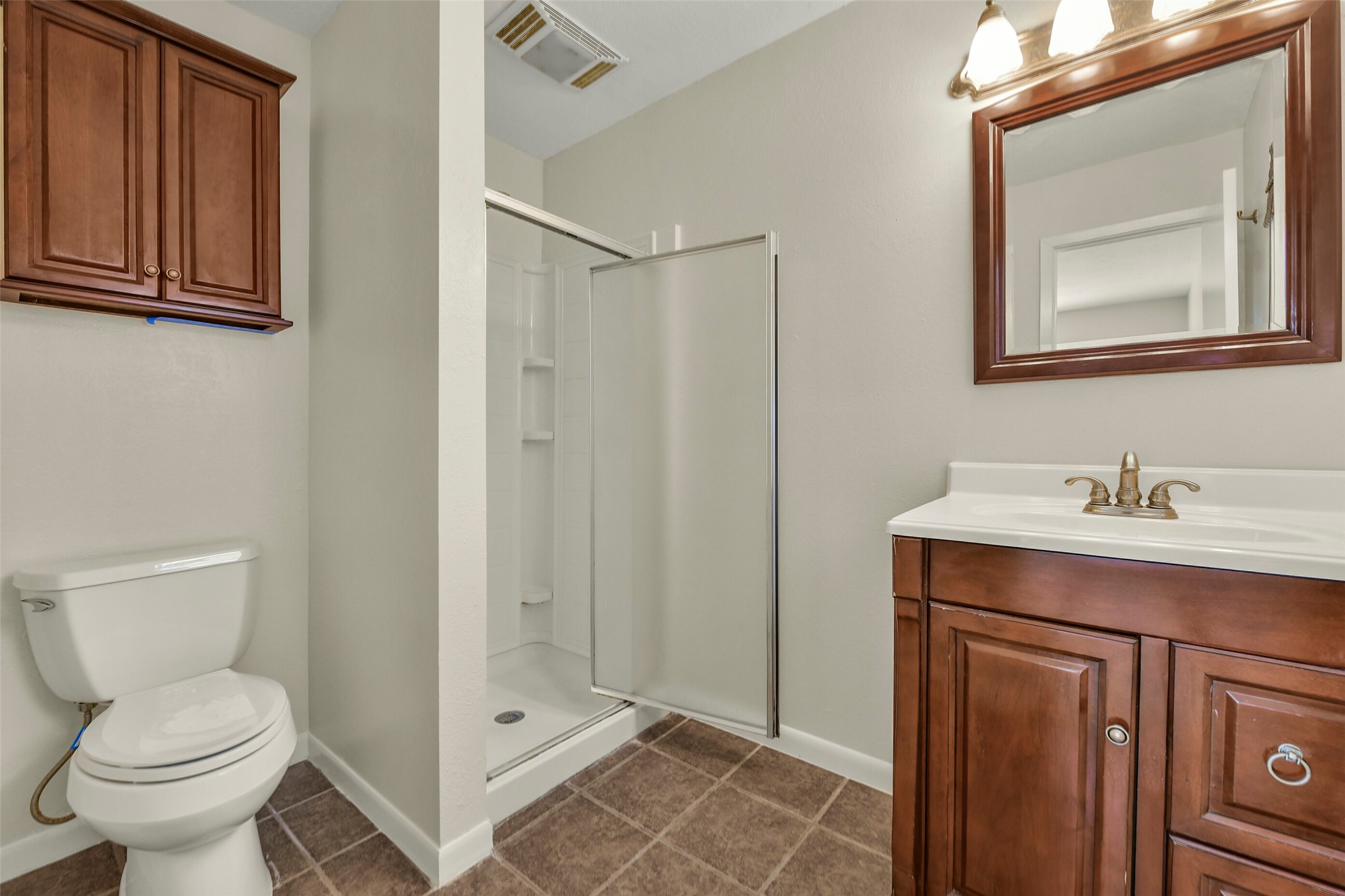 Elegant bathroom featuring a glass-enclosed shower, rich wood cabinetry, and a sleek vanity with a matching mirror, offering a blend of functionality and style.