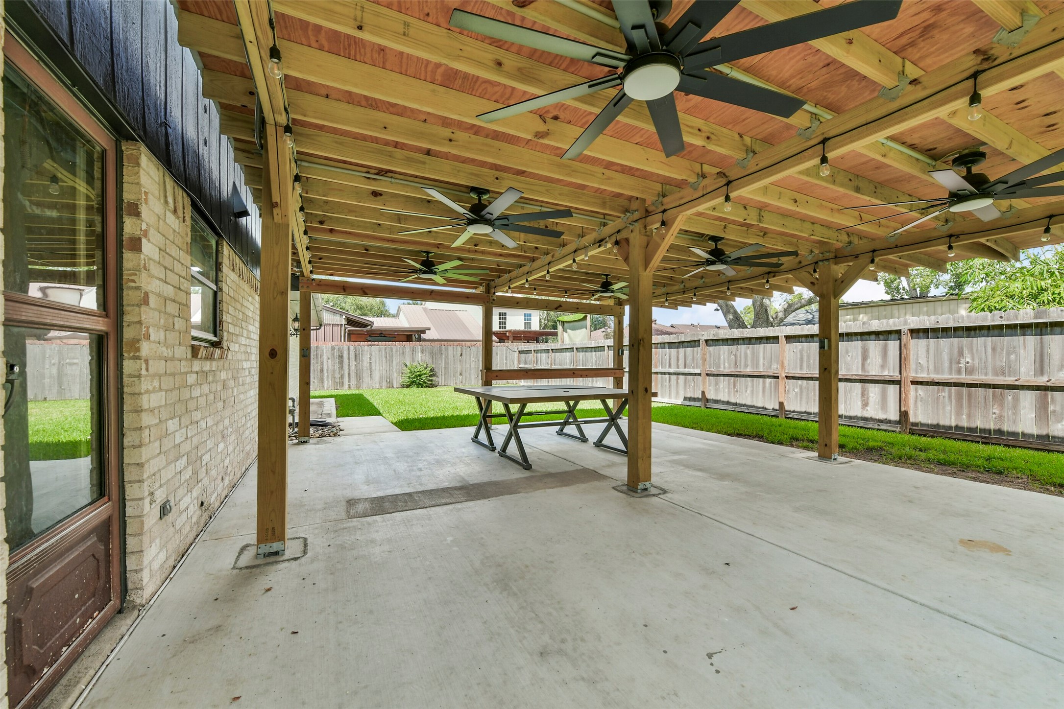 Covered patio with multiple ceiling fans, perfect for outdoor entertaining, overlooking a lush, fenced backyard.
