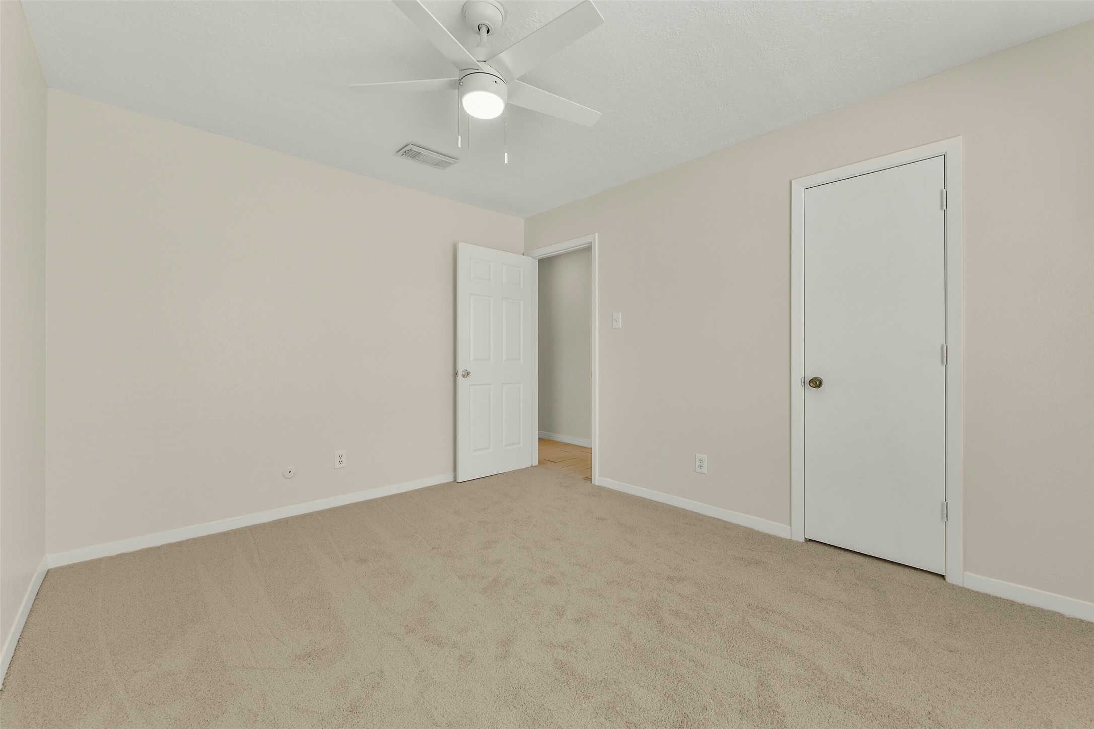 Bright and inviting, this bedroom features neutral walls, plush carpeting, and a ceiling fan, offering a comfortable and serene space.