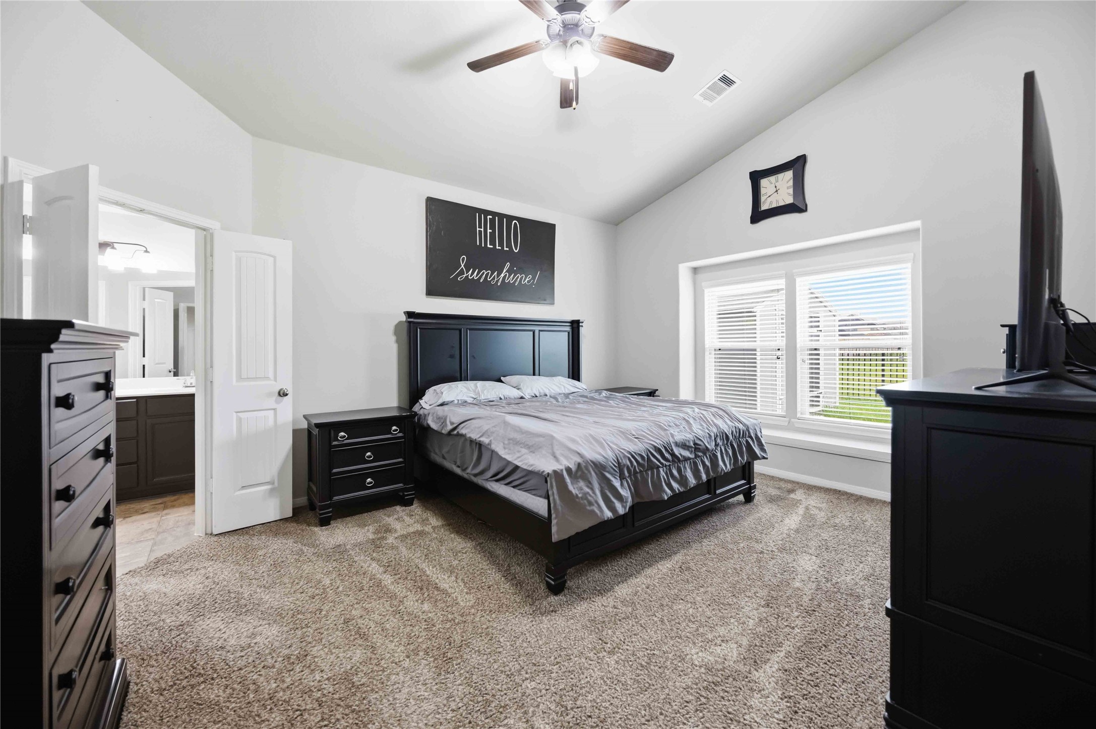 Primary bedroom with vaulted ceilings, featuring a comfortable bed, elegant dark wood furniture, and large windows that let in plenty of natural light.
