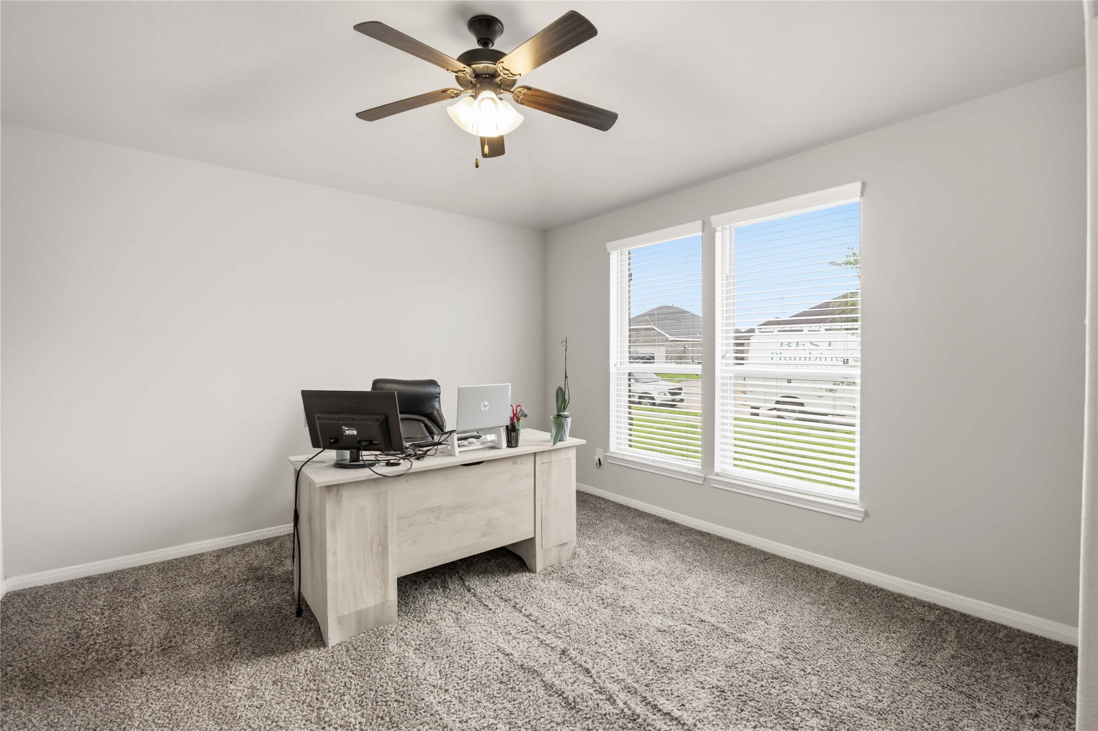 Bright and inviting home office featuring large windows, plush carpeting, and a ceiling fan for comfort. Bright and inviting home office featuring large windows, plush carpeting, and a ceiling fan for comfort.