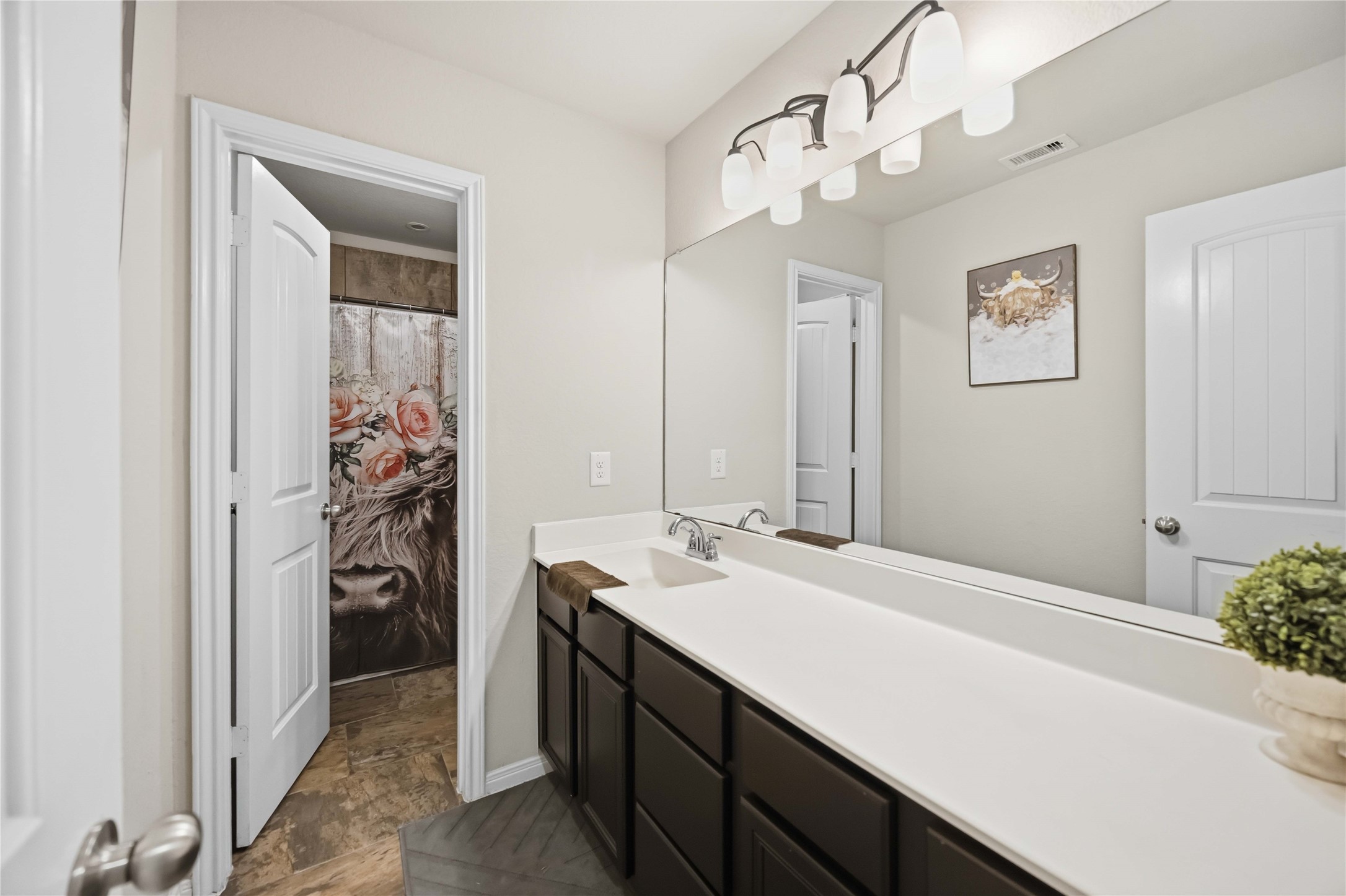 Bright and modern bathroom featuring a sleek vanity with ample storage, contemporary lighting, and a decorative shower curtain adding a touch of elegance.
