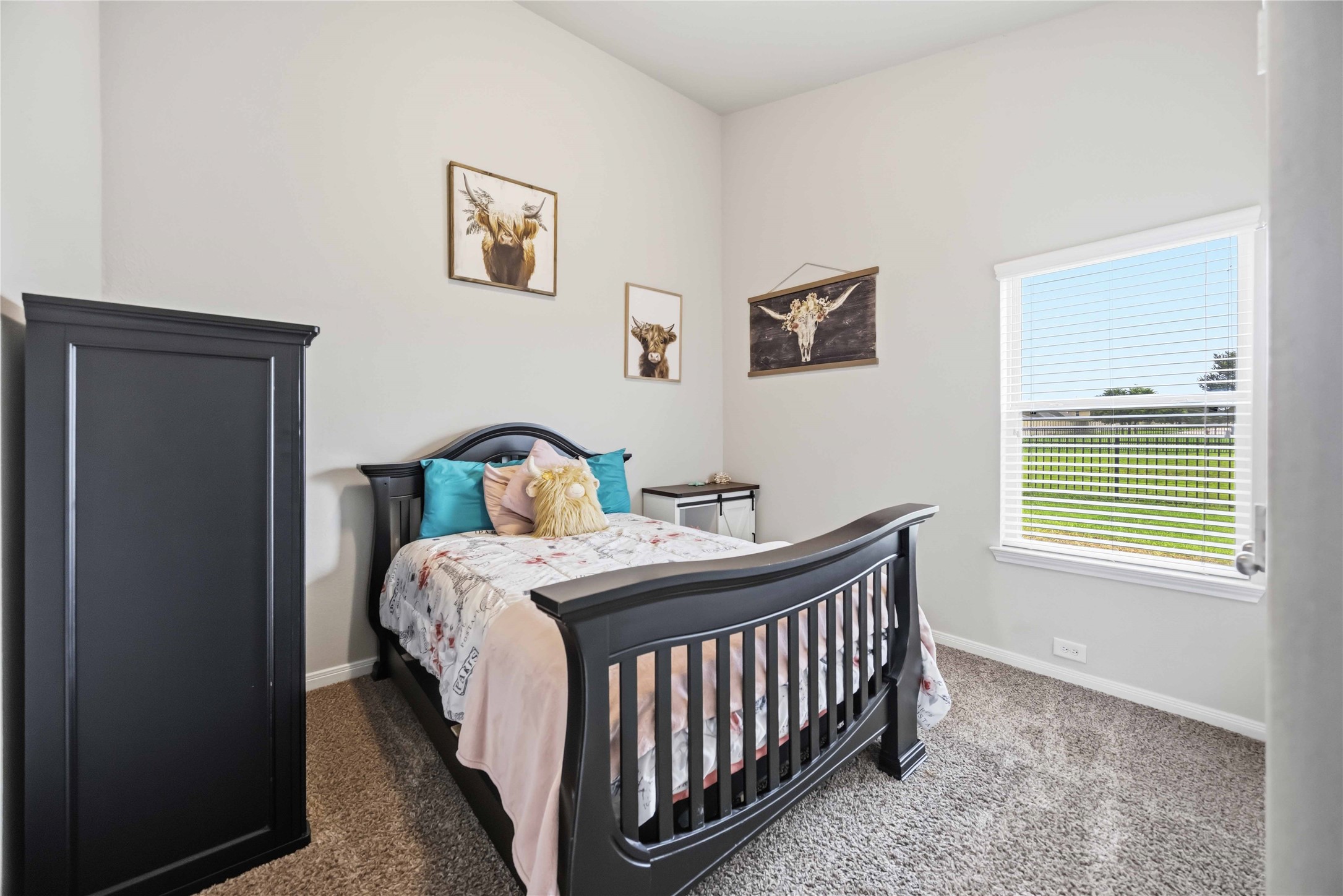 Cozy bedroom featuring a stylish dark wood bed, soft carpeting, and abundant natural light from a large window overlooking the backyard.