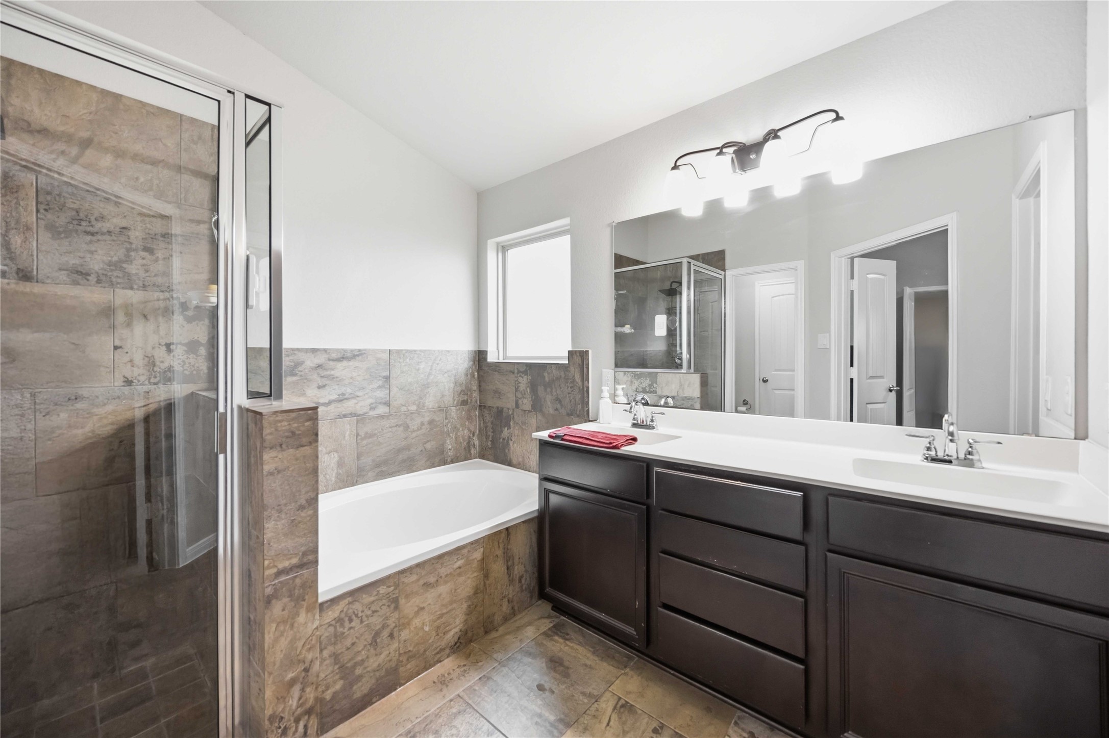 Primary bathroom featuring a luxurious soaking tub, separate glass-enclosed shower, and dual sinks with elegant dark cabinetry for ample storage.