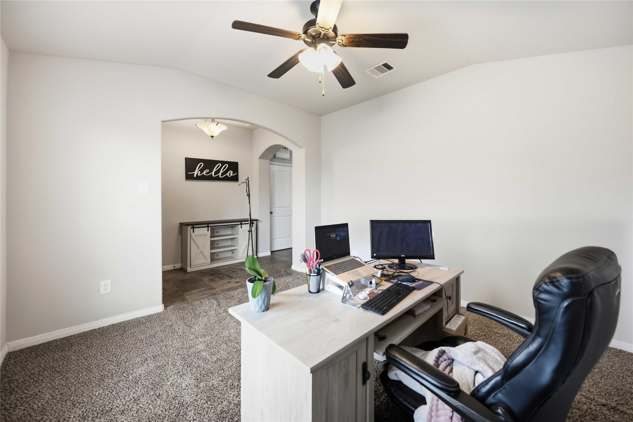 Spacious home office with plush carpeting, a ceiling fan, and a welcoming archway leading to a separate area, ideal for productivity and comfort. Spacious home office with plush carpeting, a ceiling fan, and a welcoming archway leading to a separate area, ideal for productivity and comfort.