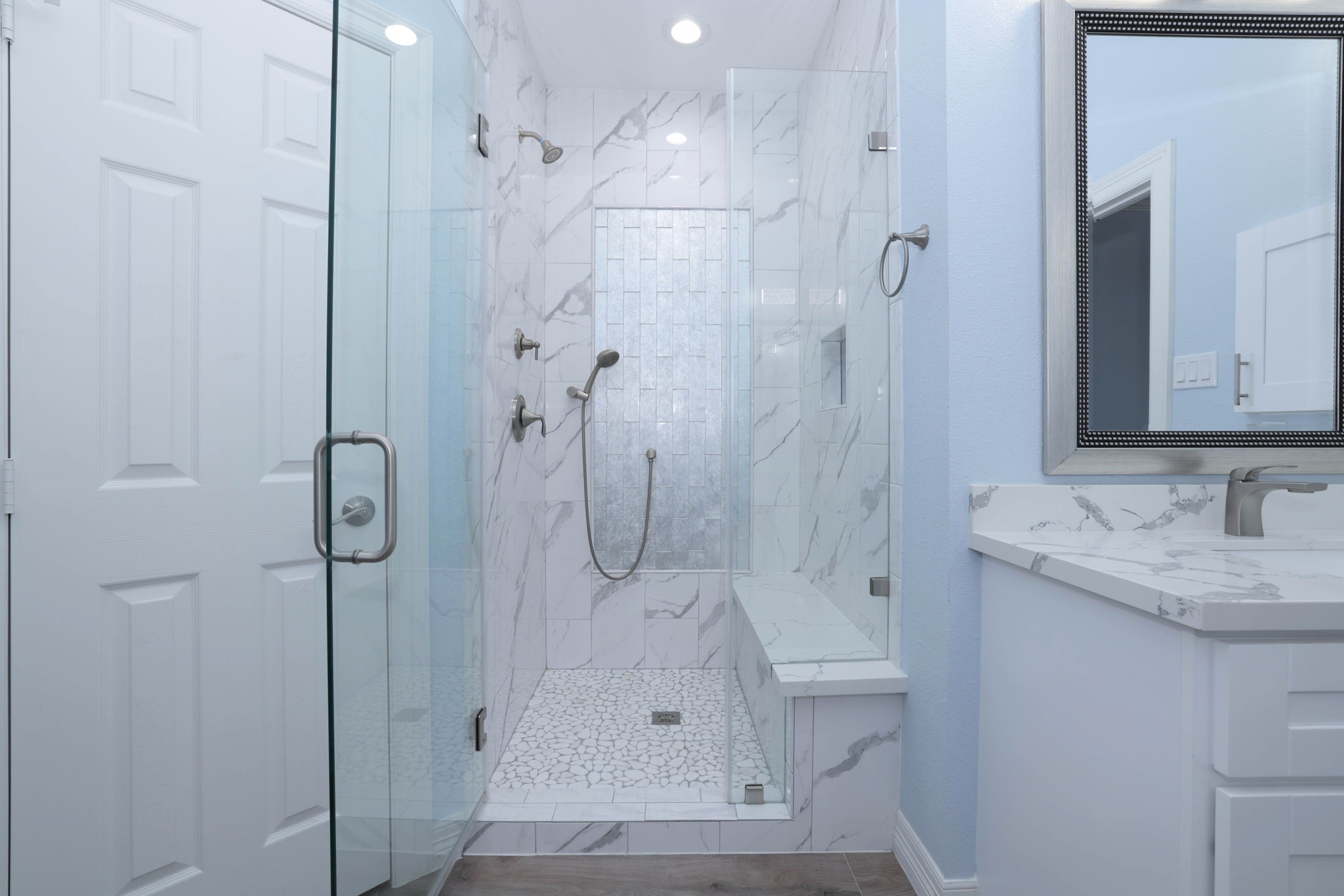 The giant shower has designer tile, a built in bench, hand held sprayer, and frameless glass door shower.