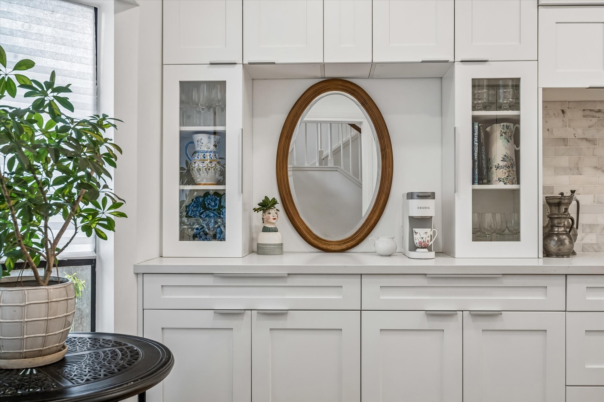 Elegant kitchen space featuring sleek white cabinetry with glass displays, a cozy coffee nook, all accented by warm natural lights.