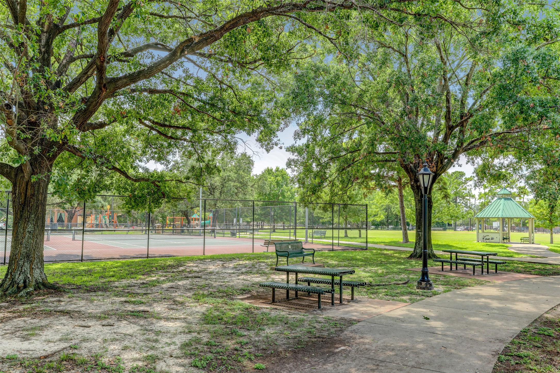 A serene park setting featuring lush trees, a playground, tennis courts, and a charming gazebo, perfect for outdoor relaxation and recreation.