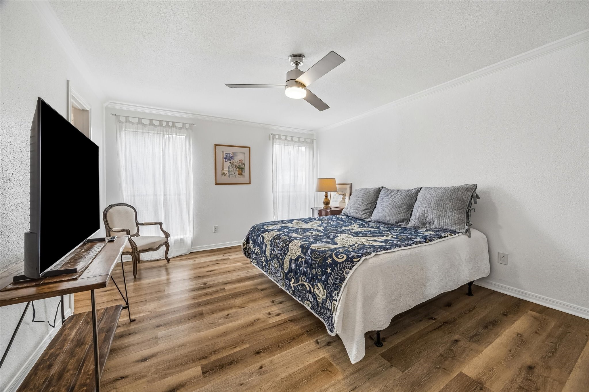 Primary bedroom featuring new vinyl plank flooring, a stylish ceiling fan, and ample natural light from large windows, creating a serene retreat.