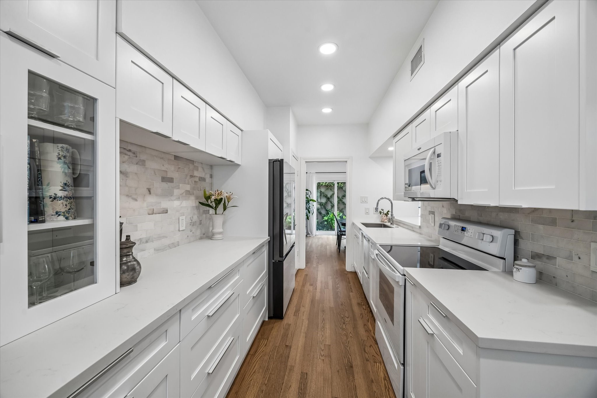 Welcome home to this beautiful galley kitchen with white cabinetry, stainless steel appliances, and a modern subway tile backsplash, complemented by warm hardwood floors and ample natural light.