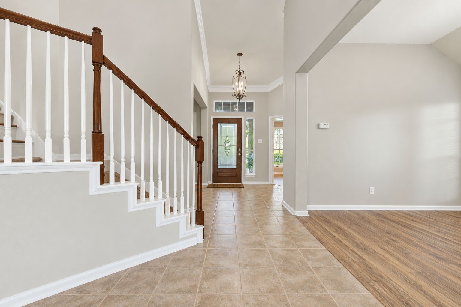 Welcoming two-story entry featuring a decorative glass front door, high ceilings, elegant light fixture, and staircase with wood accents. The open layout provides a view into the adjacent flex/bonus room. Welcoming two-story entry featuring a decorative glass front door, high ceilings, elegant light fixture, and staircase with wood accents. The open layout provides a view into the adjacent flex/bonus room.