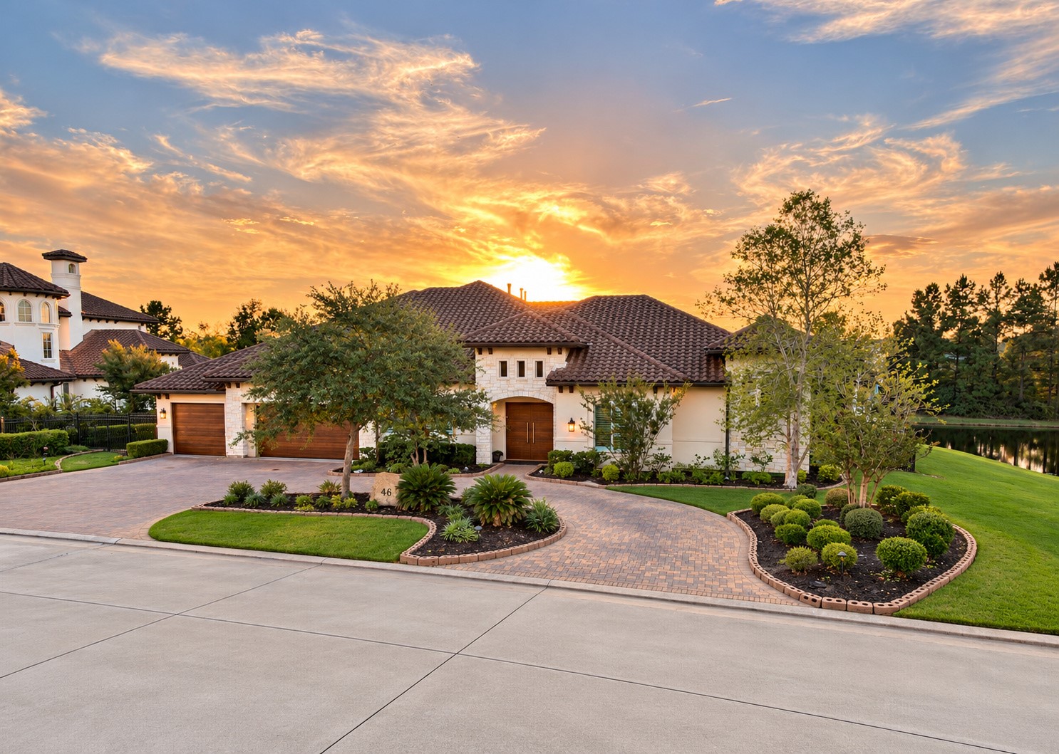 Stunning sunset views create a breathtaking backdrop for this luxury estate, showcasing its elegant architecture, circular driveway, and beautifully landscaped grounds.