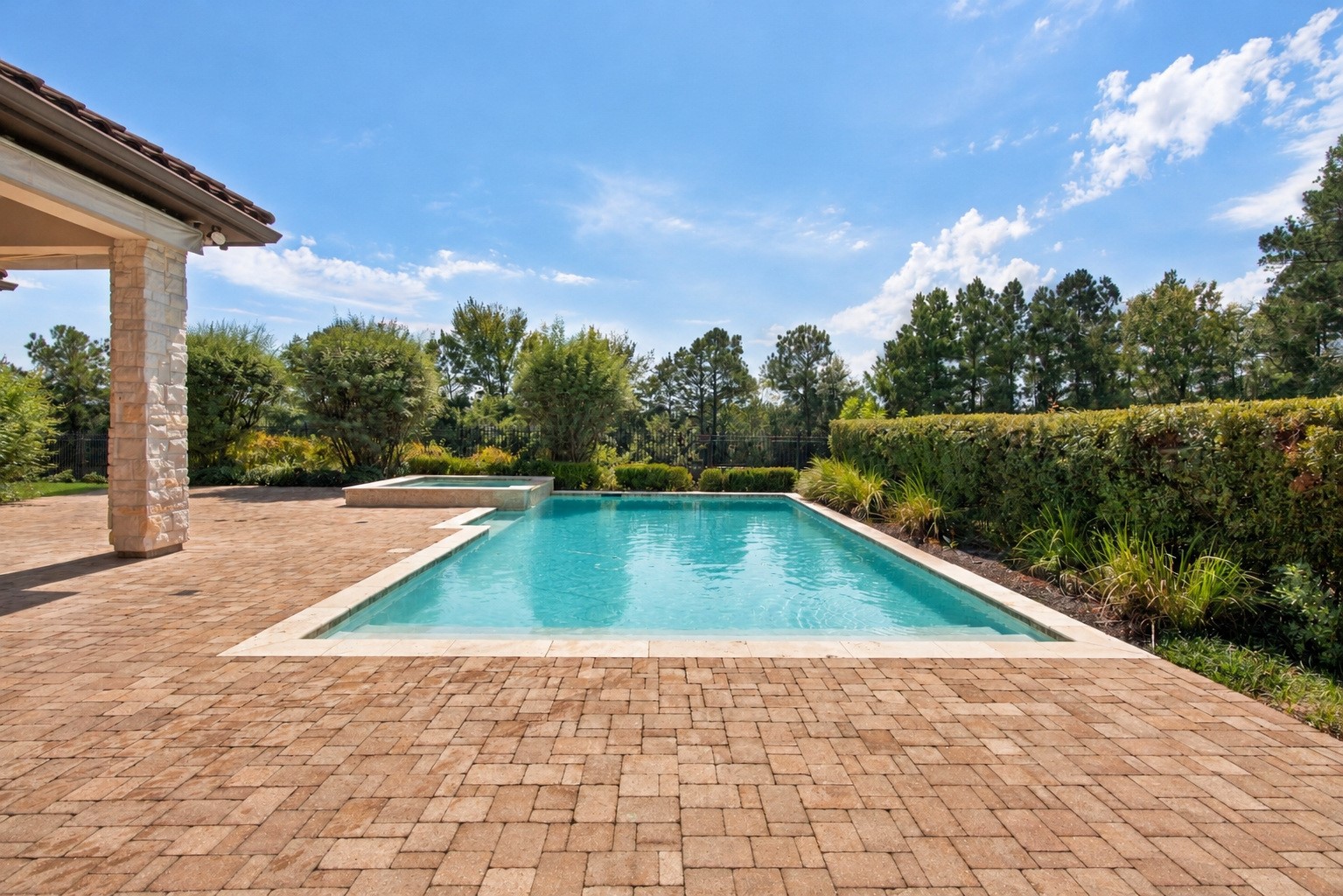 Sparkling pool and spa surrounded by an expansive paver patio, lush landscaping, and beautiful wooded viewsan inviting backyard retreat!