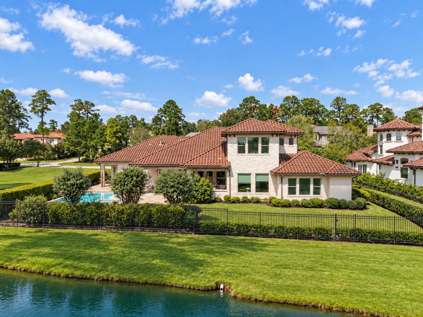 Beautiful rear elevation overlooking the water, featuring lush green lawns, mature landscaping, and an exceptional waterfront setting.