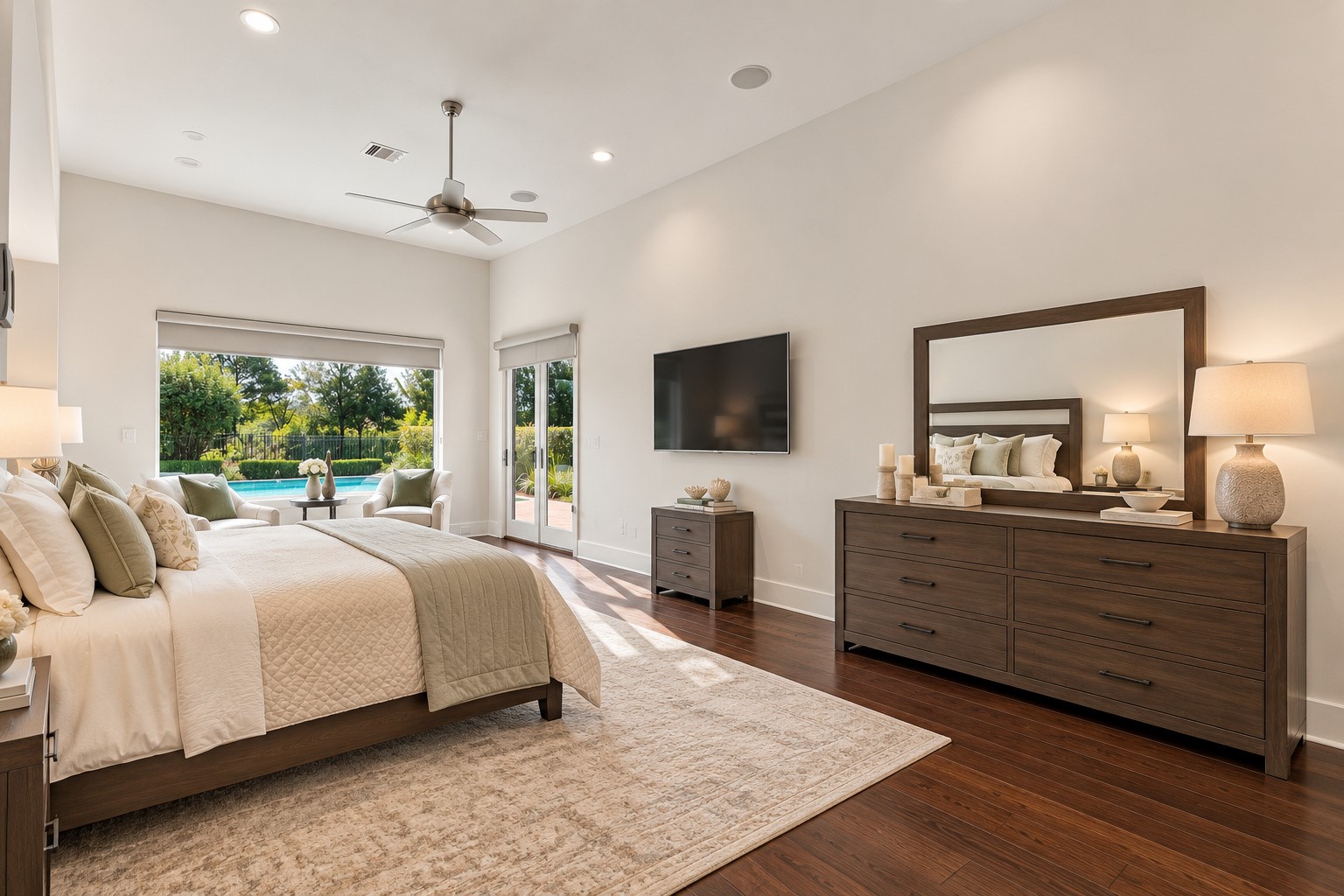 Doors open directly to the backyard pool area from this luxurious primary suite, featuring soaring ceilings, elegant finishes, a spacious sitting area, and beautiful views of the backyard oasis.