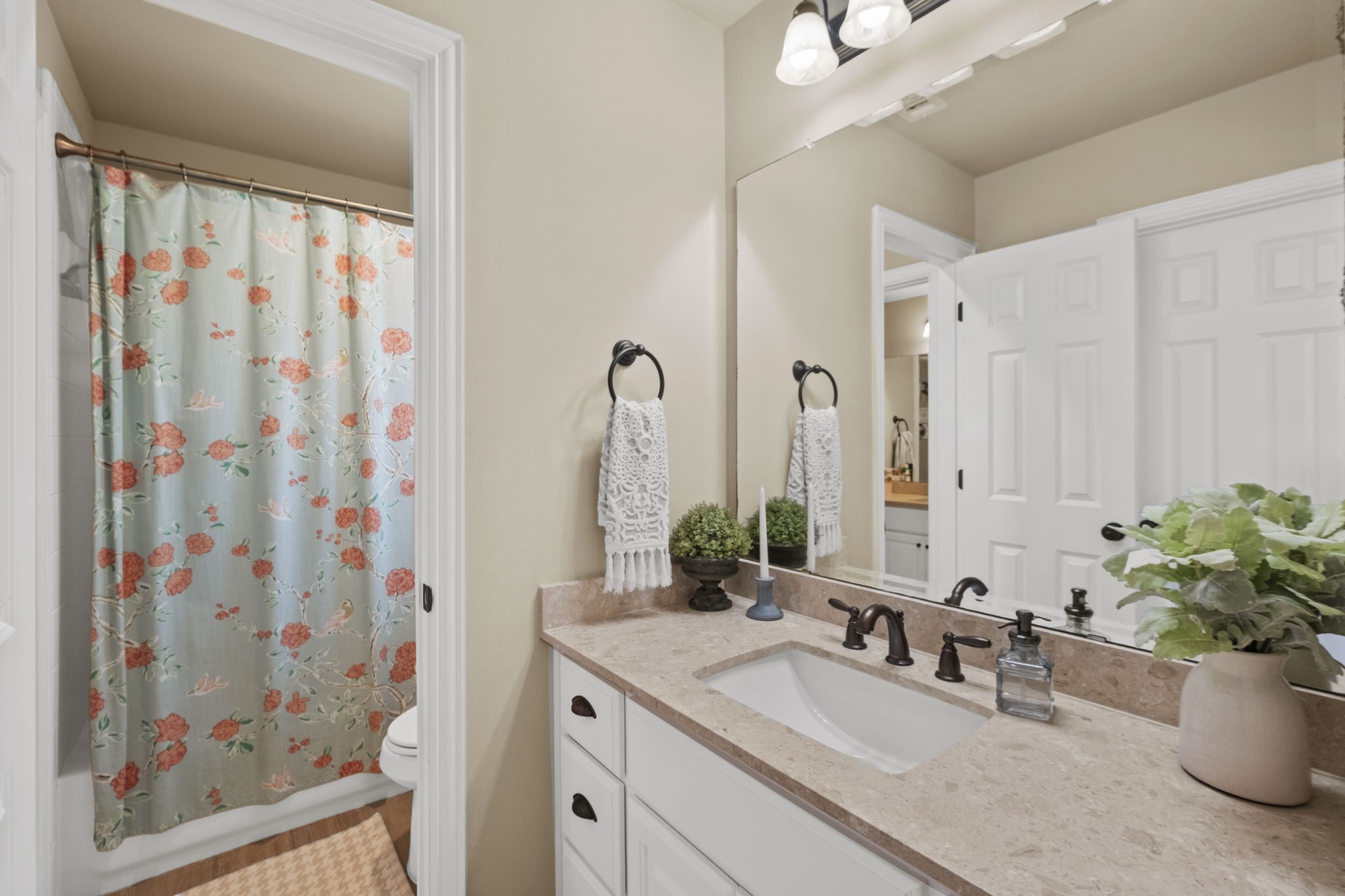 Upstairs bathroom vanity area featuring a single sink set in a neutral stone-look countertop, white cabinetry with dark cup pulls, oil-rubbed bronze fixtures, a full mirror with light bar, and an enclosed door leading to the toilet and tub/shower combination.