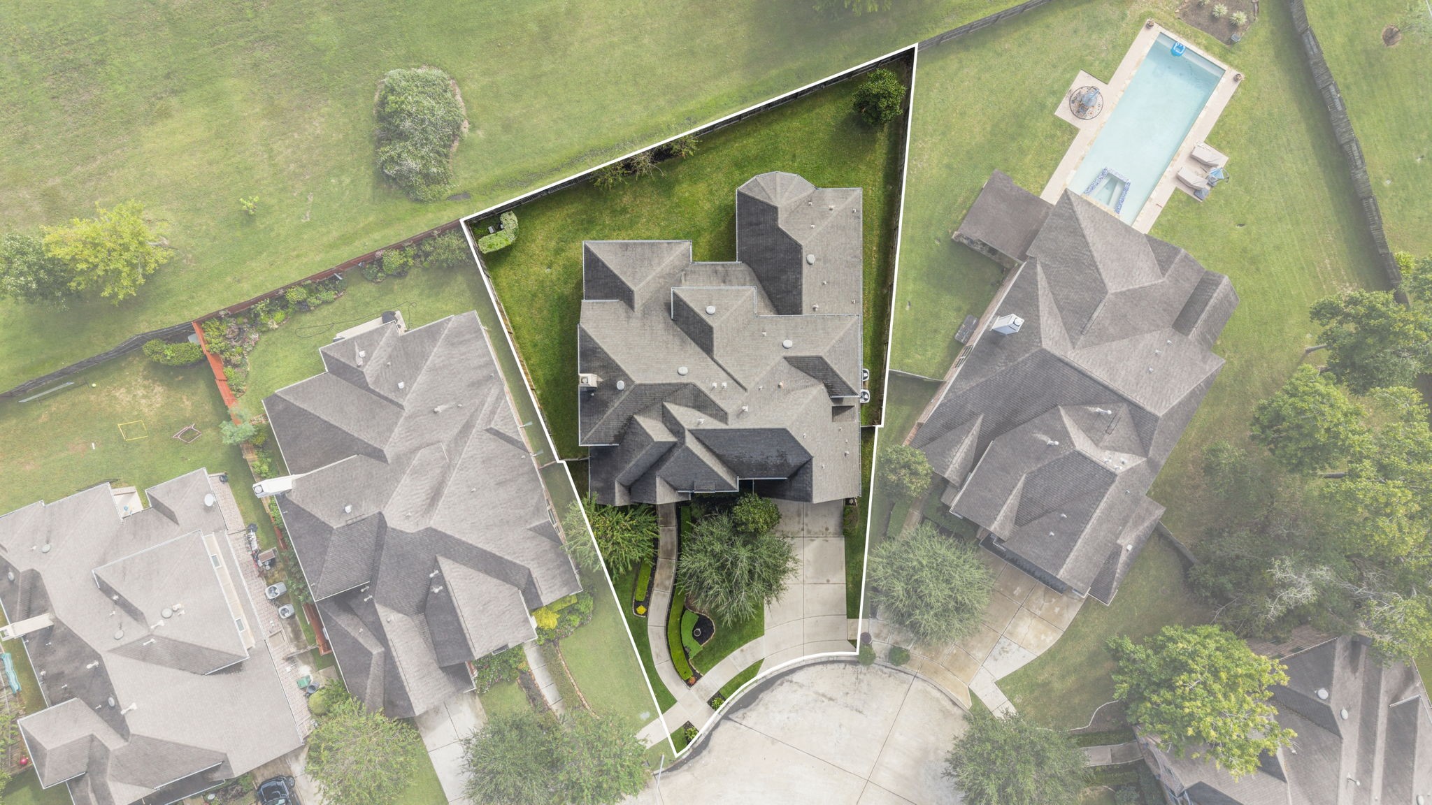Direct overhead birds-eye aerial perspective detailing the full property boundary outline, complex shingled roofline design, concrete driveway, front walkway landscaping, and fully fenced grassy backyard.
