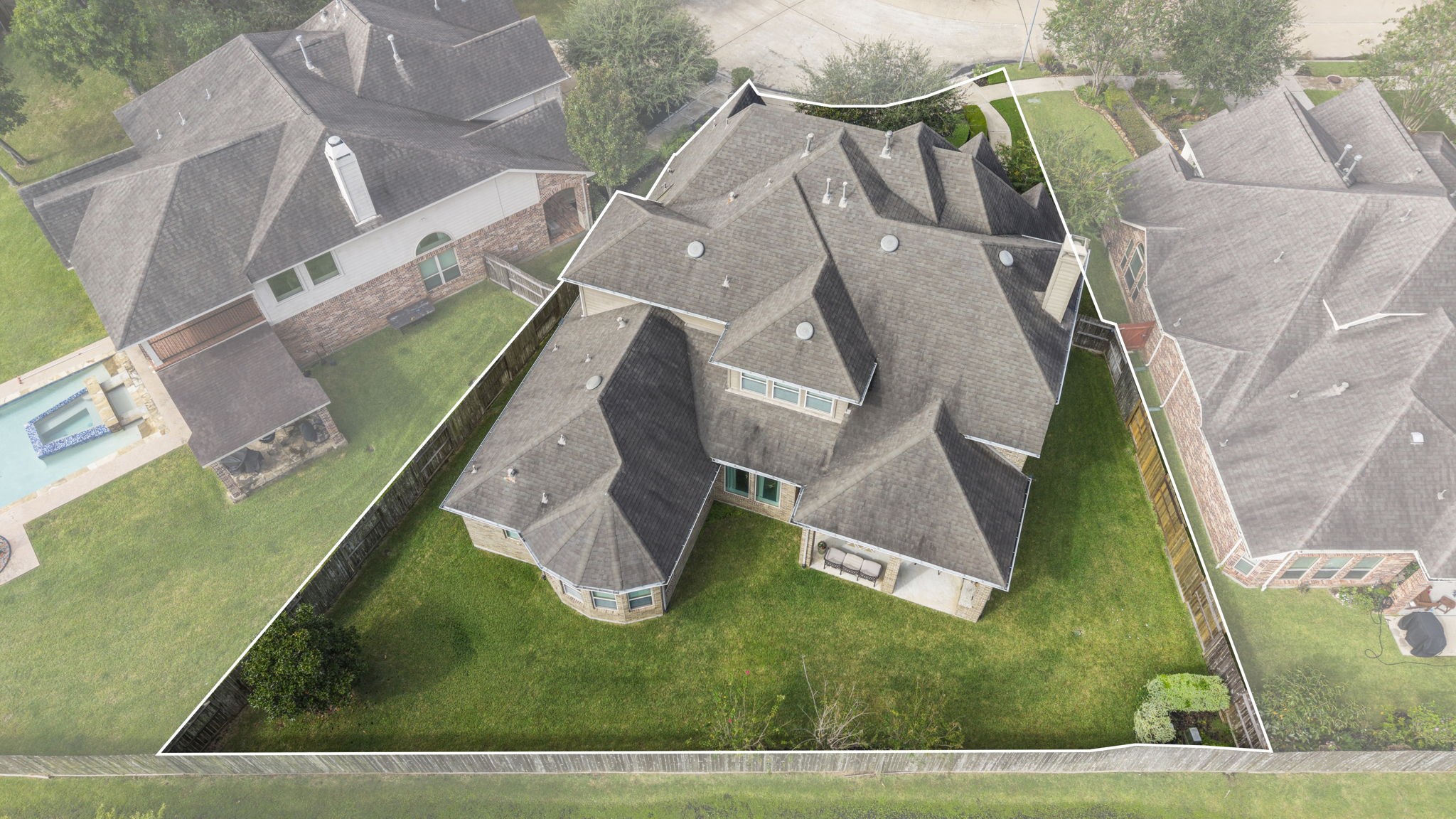 Elevated rear aerial angle featuring a highlighted boundary line around the backyard, showcasing the full lot footprint, rear elevation brickwork, bay window section, and large covered patio.