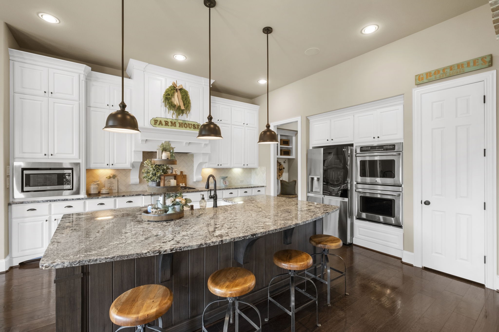 Functional kitchen perspective showing double wall ovens, a built-in microwave surround, integrated stainless steel appliances, and a walk-in pantry door. Highlights the extensive granite counter space and raised panel cabinet layout.